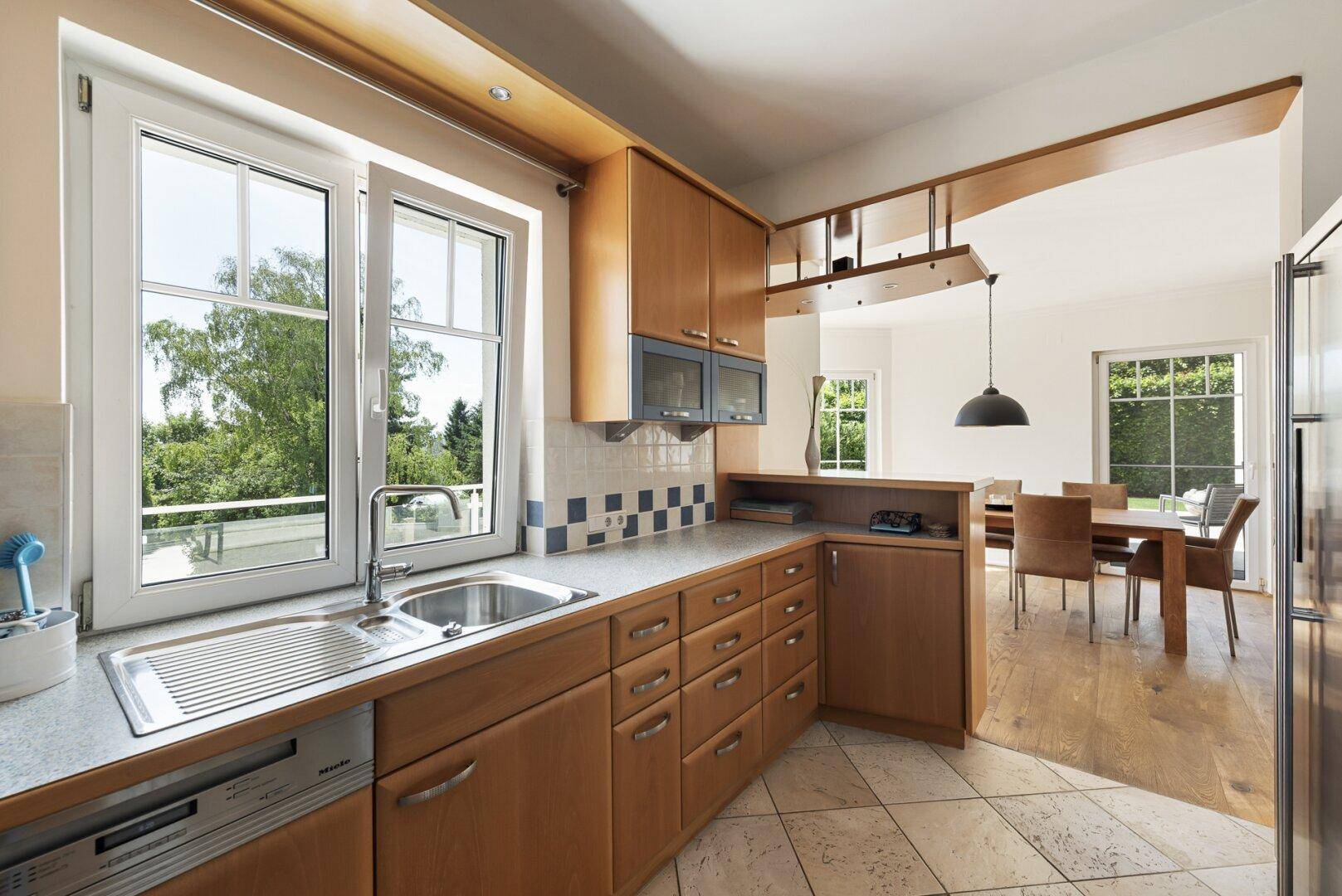 Funktionale Küche mit Holzschränken, gefliestem Boden und Blick ins Grüne durch das Fenster.