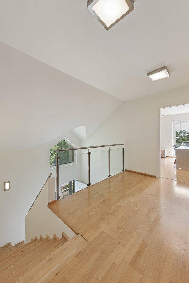 Heller Flur im Obergeschoss mit Holzboden, Glasgeländer und Blick auf die untere Etage.