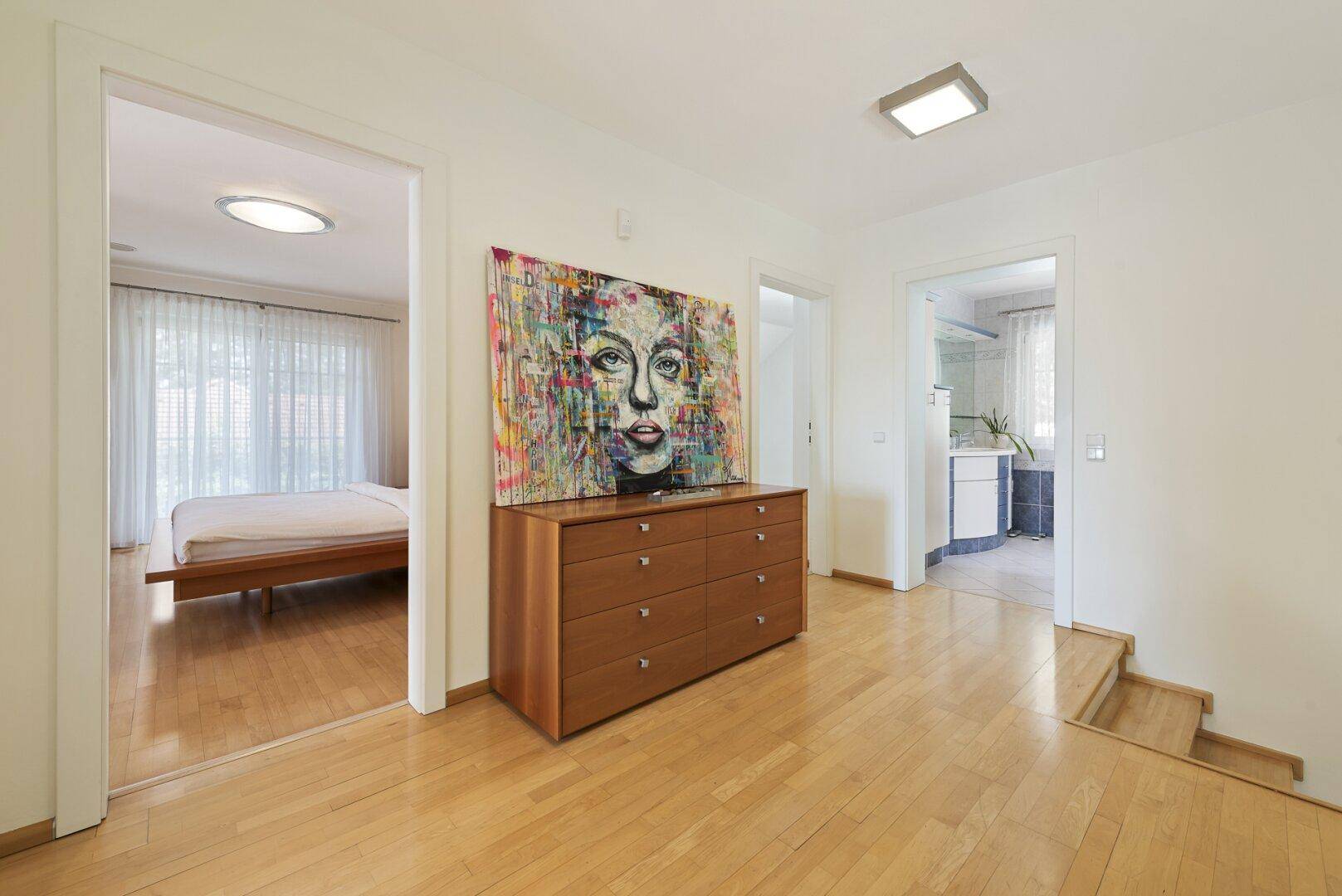 Heller Flur im Obergeschoss mit Holzboden, Kunstwerk und Zugang zu Schlafzimmer und Bad.