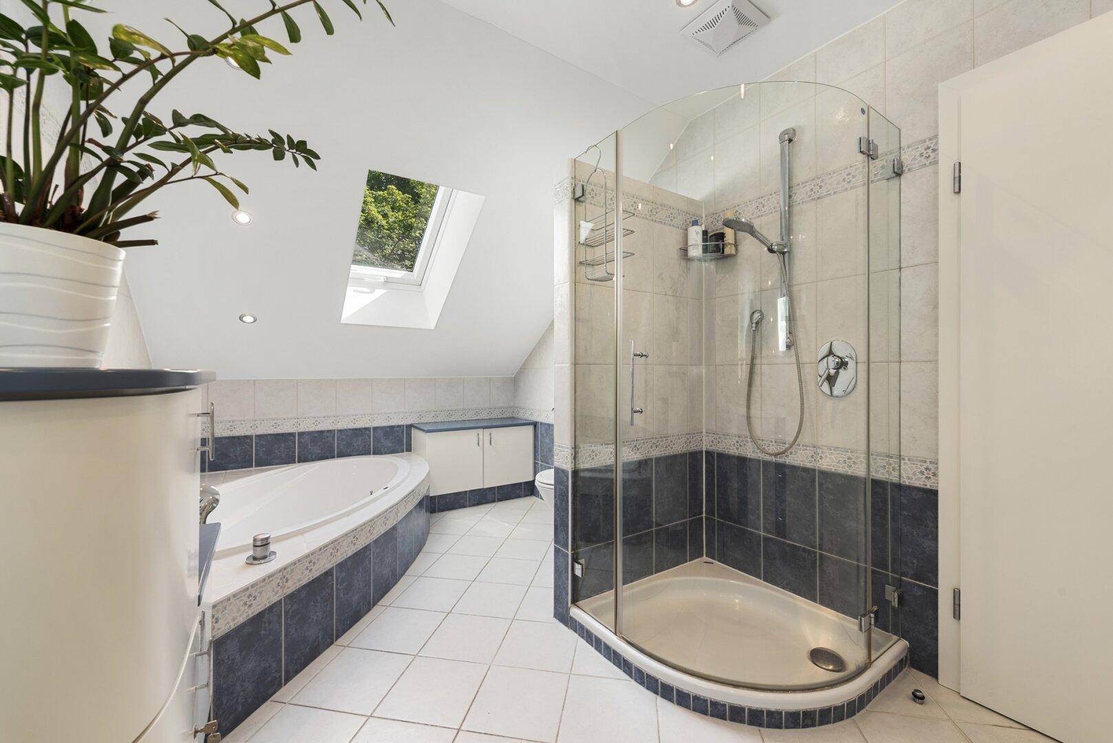 Modernes Badezimmer mit Badewanne, Duschkabine, Dachfenster und blauen Akzentfliesen.
