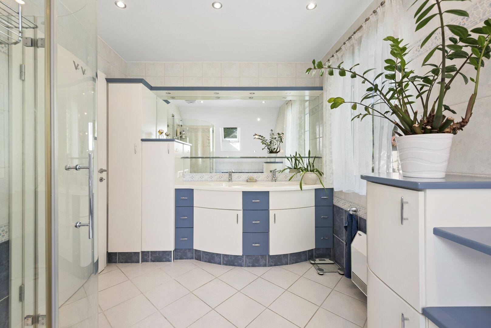 Helles Badezimmer mit Doppelwaschbecken, Dusche und blauen Akzenten.