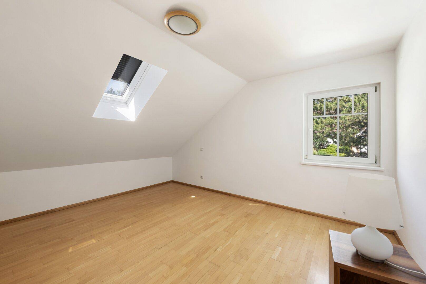 Helles Dachzimmer mit Holzboden und Dachfenster, ideal als Schlaf- oder Arbeitszimmer.