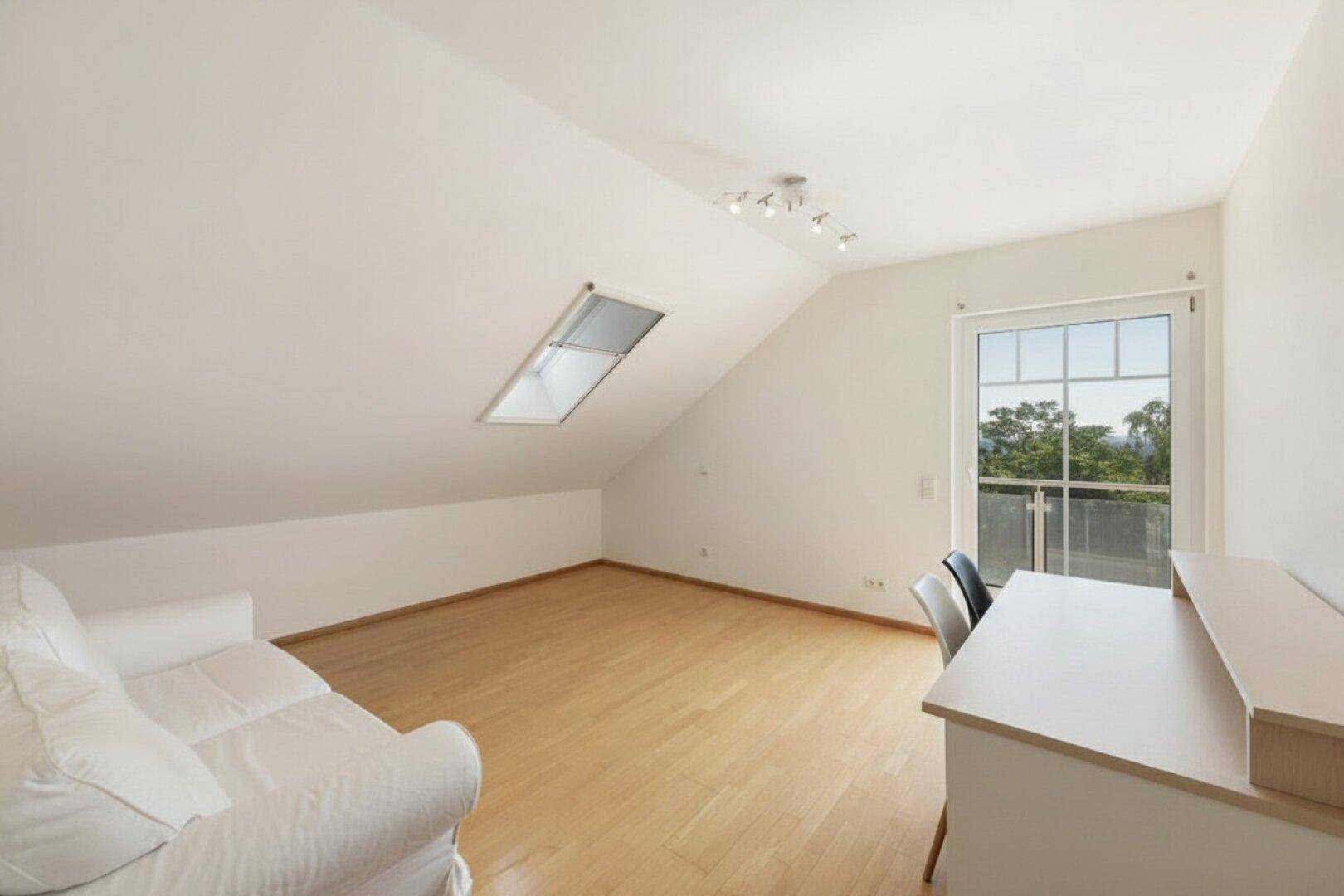 Geräumiges Dachzimmer mit Holzboden, Dachfenster und Zugang zu einem französischen Balkon.