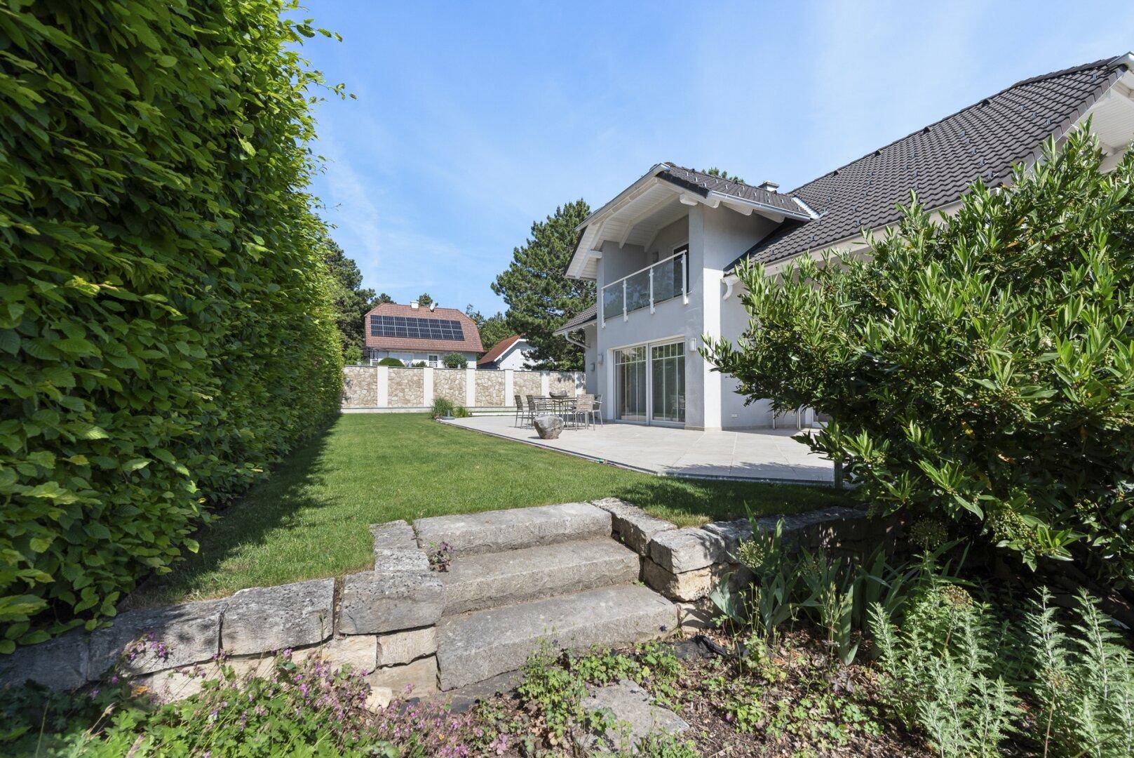 Gepflegter Garten mit Rasenfläche, Terrasse und Blick auf das moderne Wohnhaus.