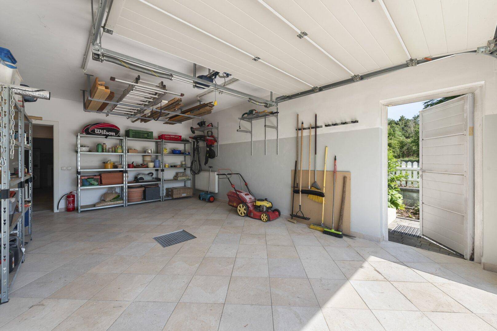 Geräumige Garage mit Fliesenboden, Regalen und direktem Zugang zum Garten.