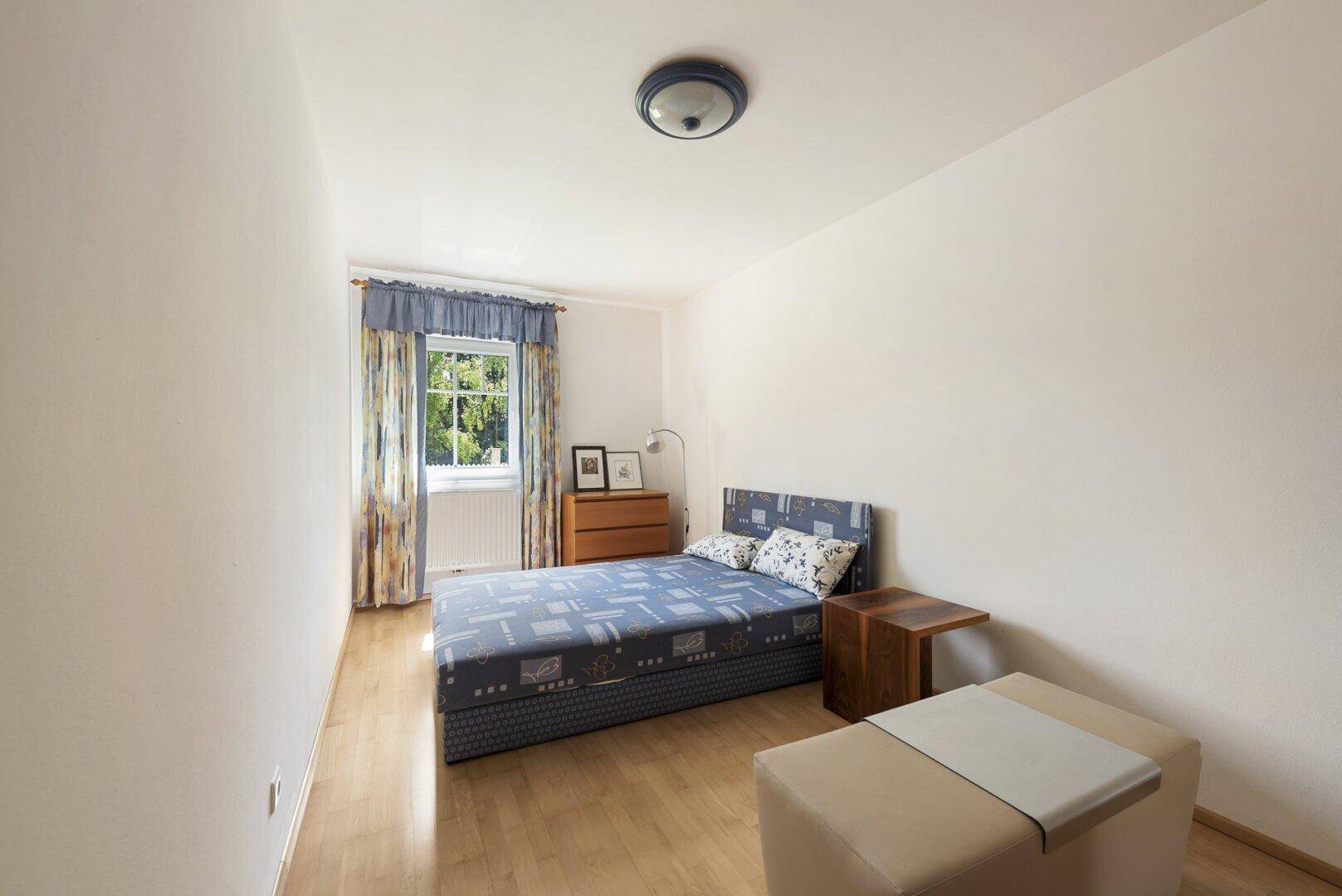 Gemütliches Schlafzimmer mit Holzboden, Fenster und einfacher Einrichtung.