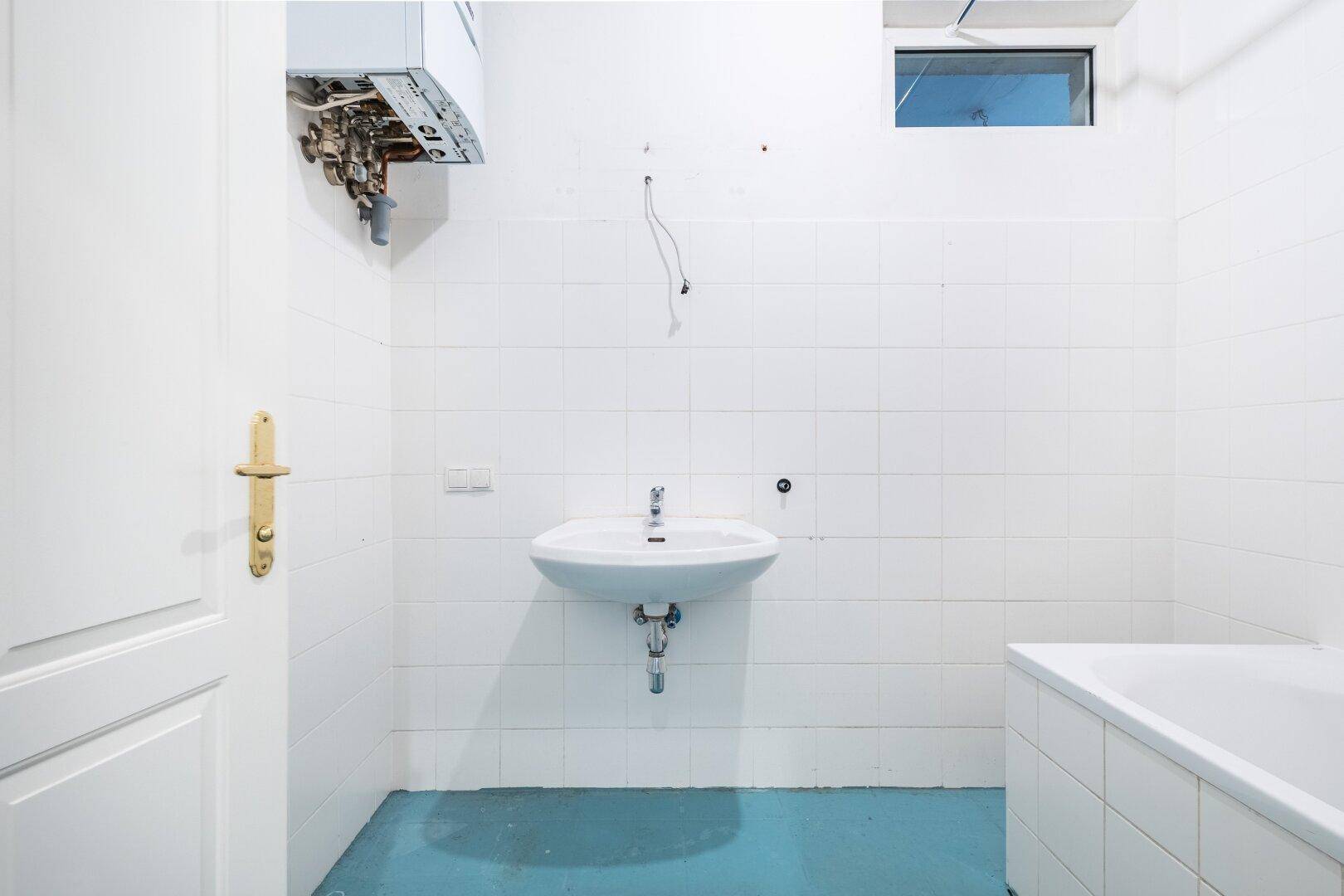 Badezimmer mit weißen Fliesen, Waschbecken, Badewanne und Warmwasserbereiter.