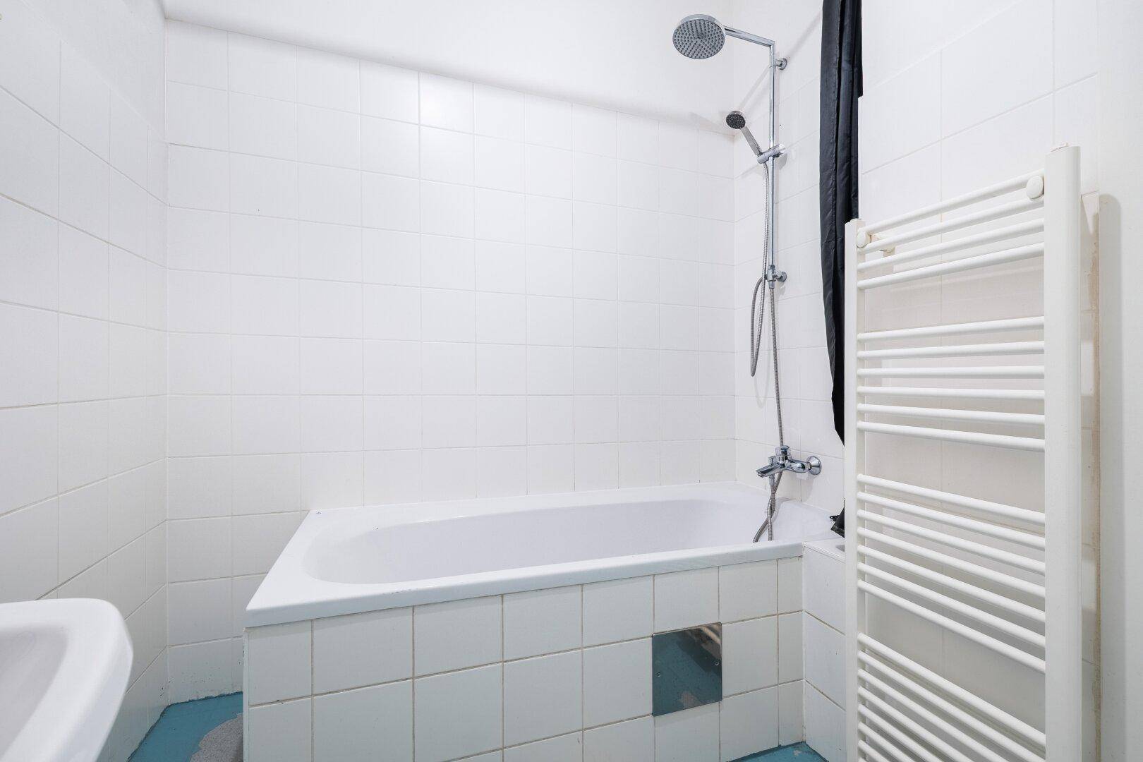 Badezimmer mit weißen Fliesen, Badewanne mit Duschfunktion und beheiztem Handtuchhalter.