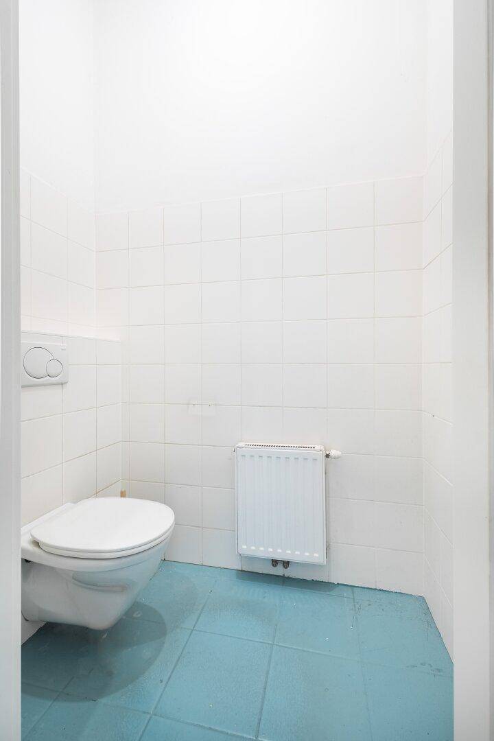 Separates WC mit weißen Fliesen, wandhängender Toilette und Heizkörper.
