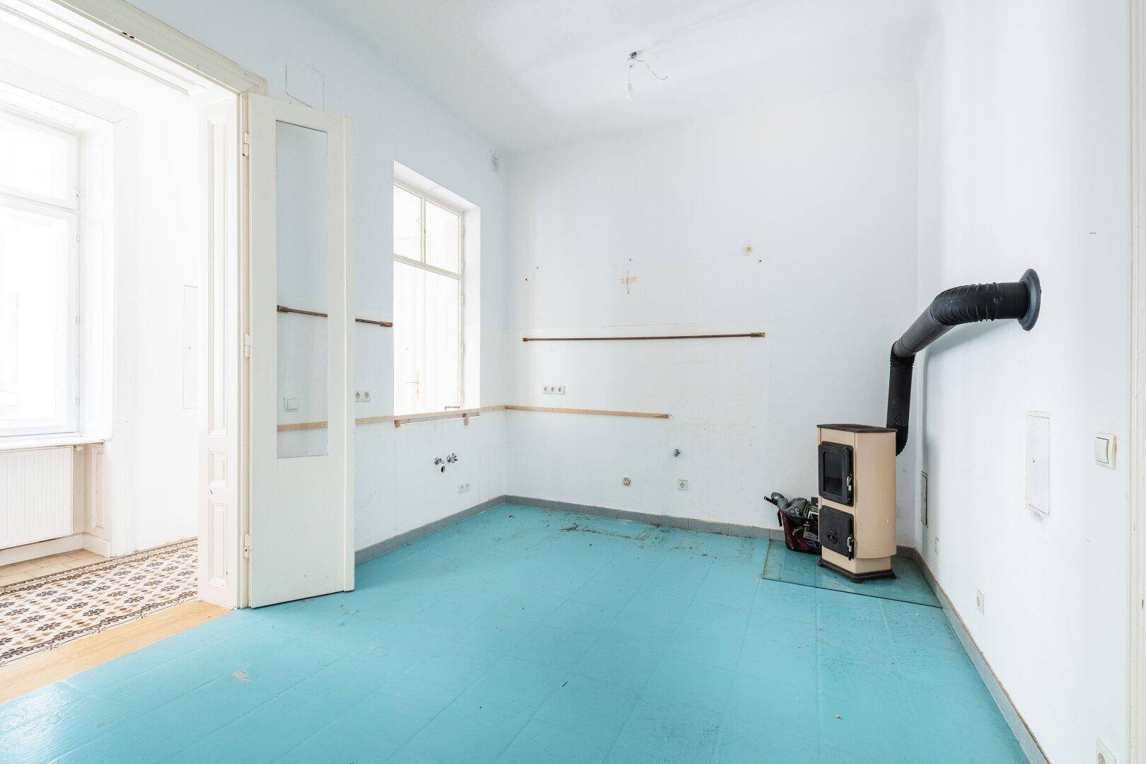 Raum mit blauem Boden, einem Ofen und Fenster, bereit für die Kücheninstallation.