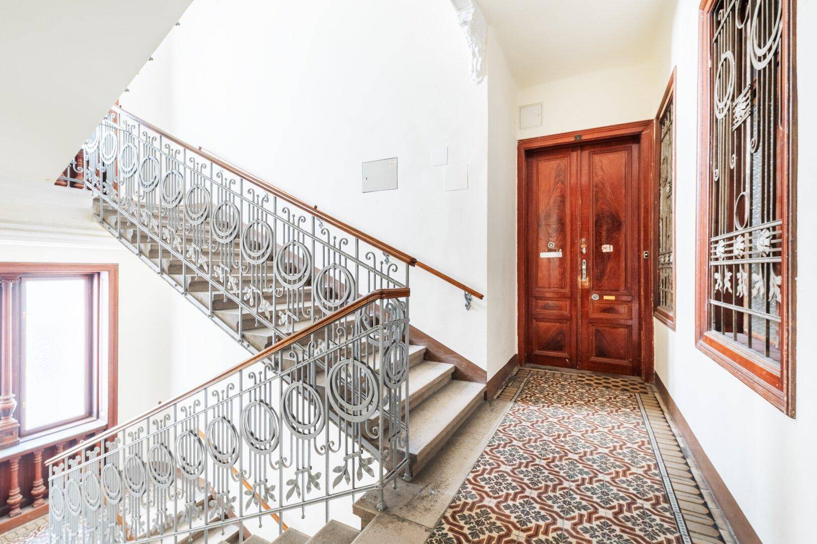 Repräsentatives Treppenhaus eines Altbaus mit kunstvollem Geländer und gemusterten Fliesen.