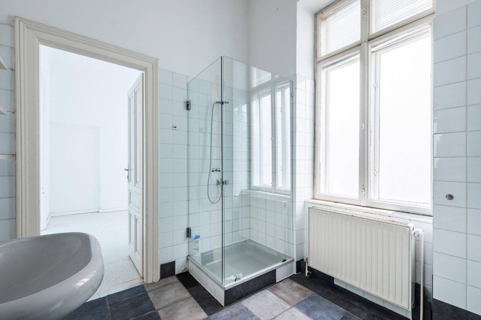 Badezimmer mit Duschkabine, Badewanne und Fenster, bereit zur Modernisierung.