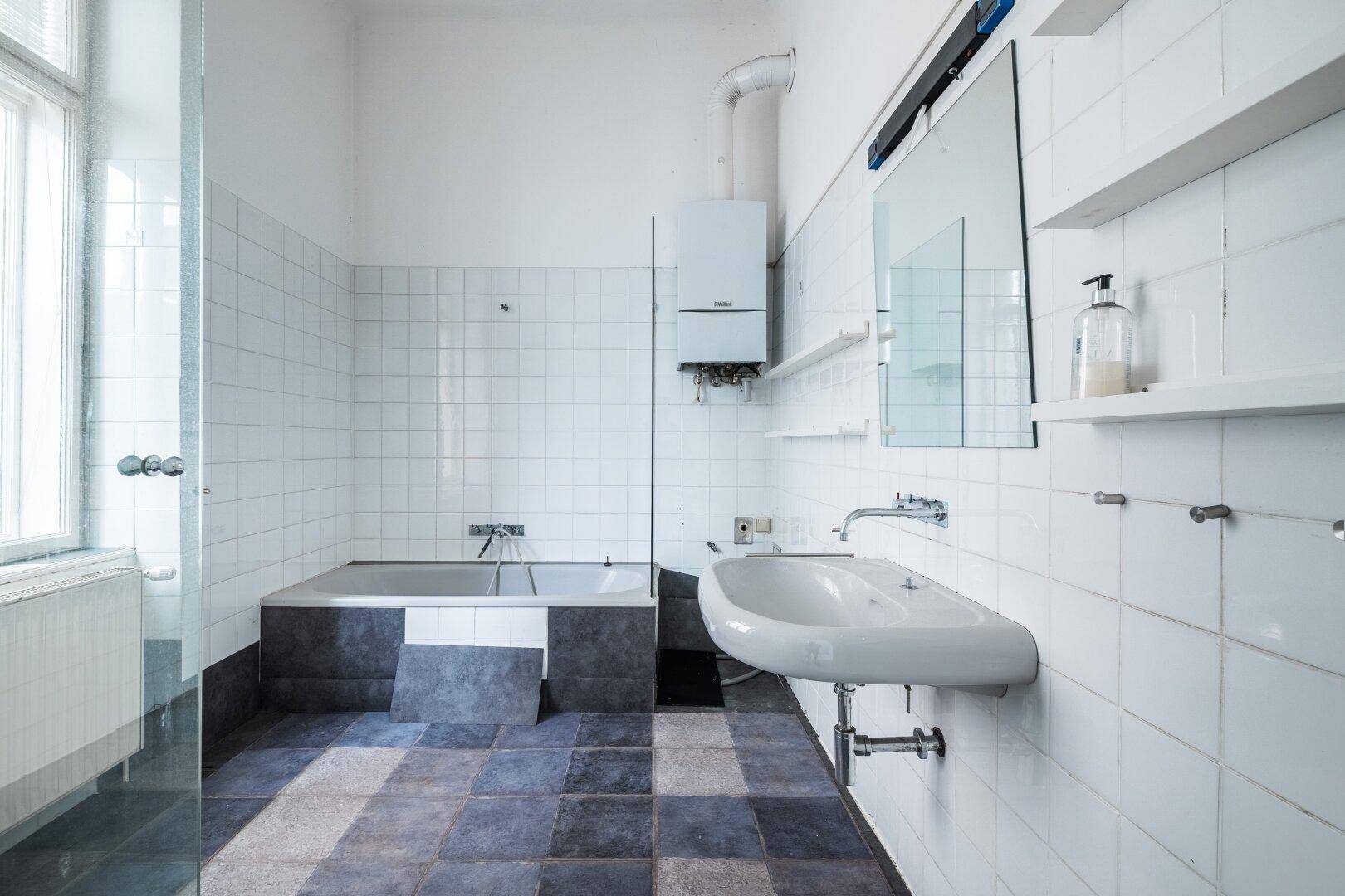 Helles Badezimmer mit Badewanne, Waschbecken und Duschkabine, gefliest in Weiß und Grau.