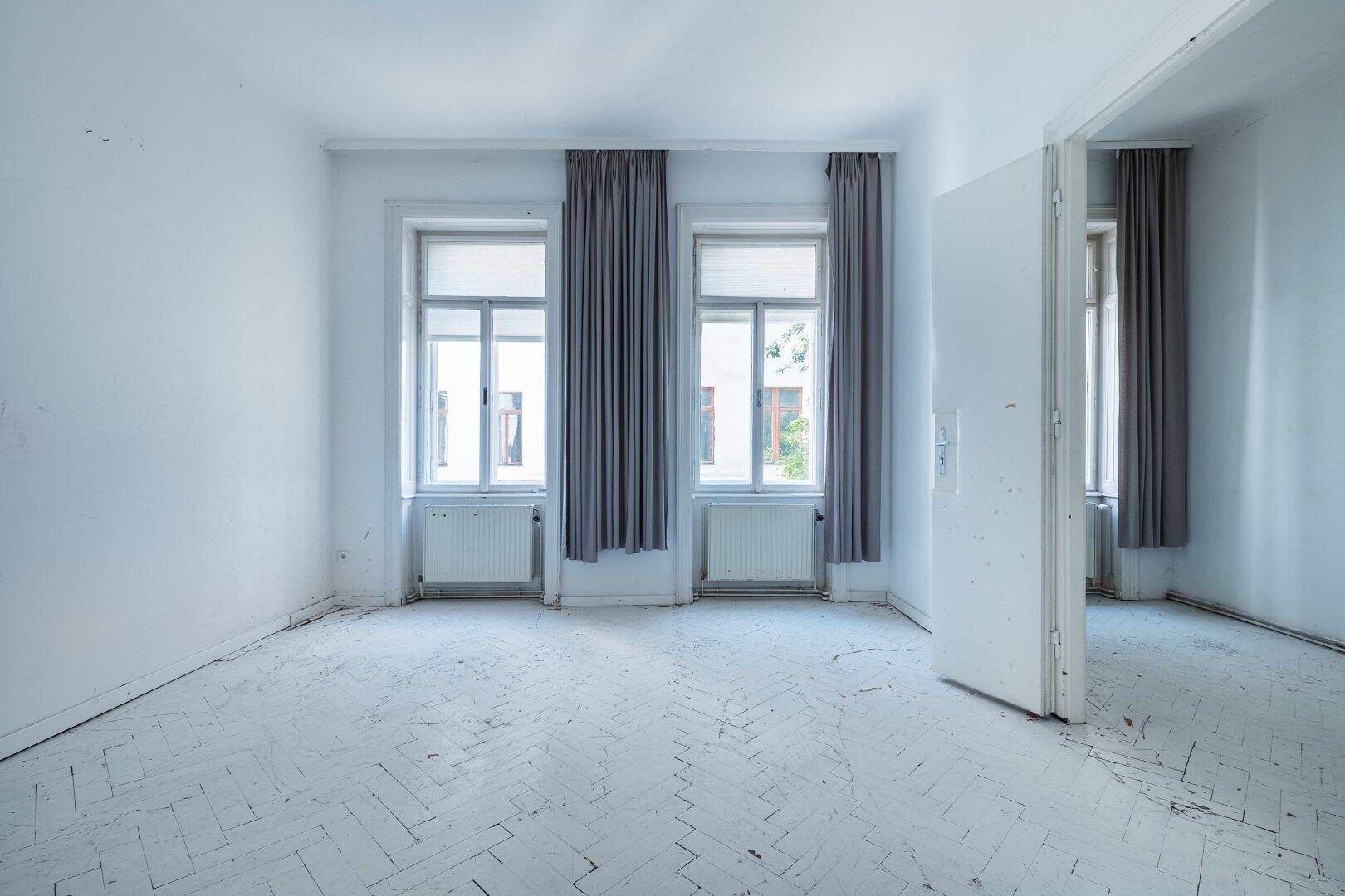 Geräumiges Zimmer mit Fischgrätparkett, hohen Fenstern und Blick ins Grüne.