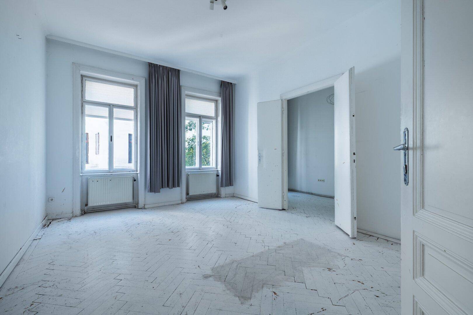 Geräumiges Zimmer mit Fischgrätparkett, hohen Fenstern und Blick ins Grüne.
