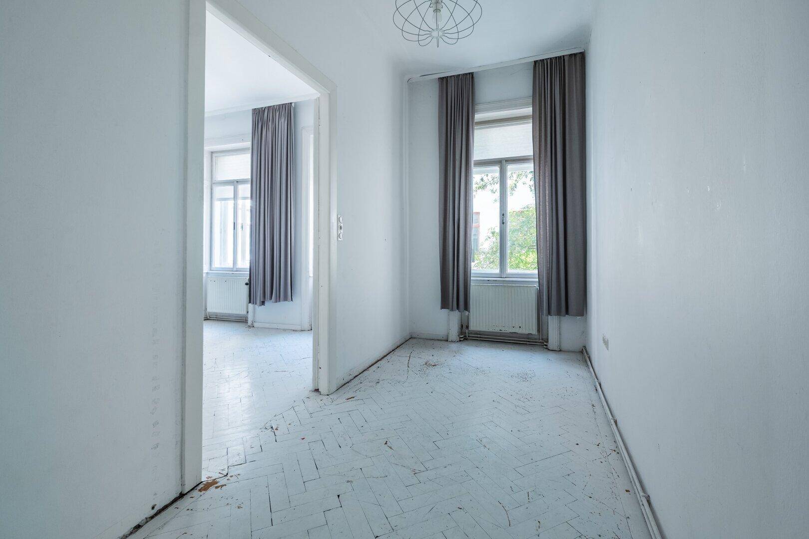Helles Zimmer mit Fischgrätparkett und hohen Fenstern, bereit zur individuellen Gestaltung.