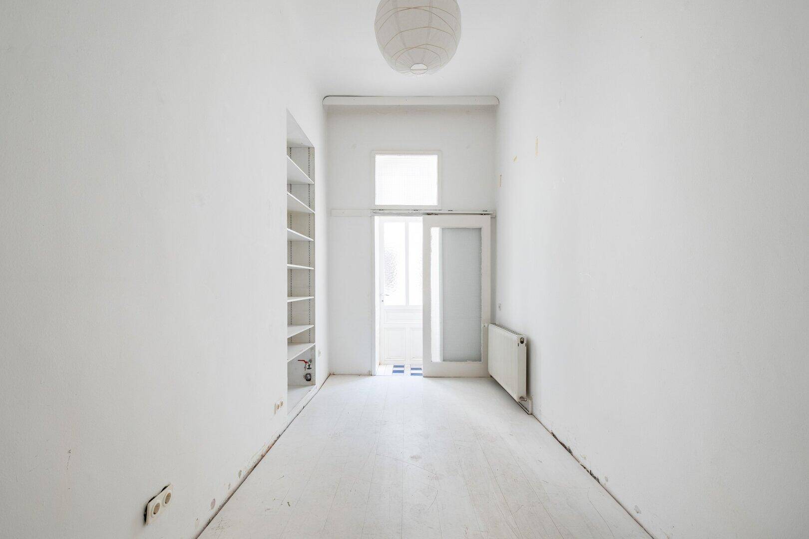 Langer, schmaler Raum mit weiß gestrichenem Fischgrätparkett und Zugang zu einem Balkon.