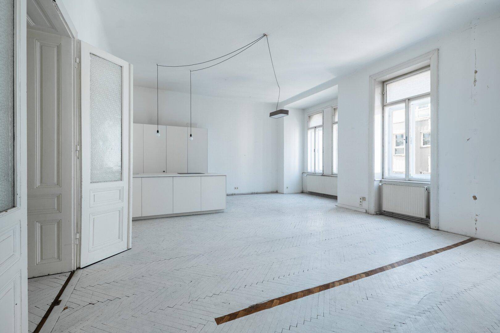 Geräumiger offener Wohnbereich mit Küchenzeile und hohen Fenstern, ideal für modernes Wohnen.