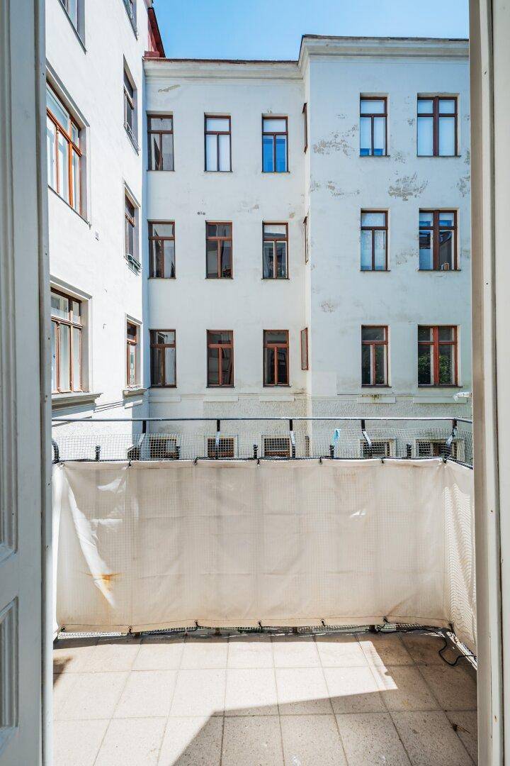 Kleiner Balkon mit Blick auf den Innenhof und die umliegenden Altbaufassaden.