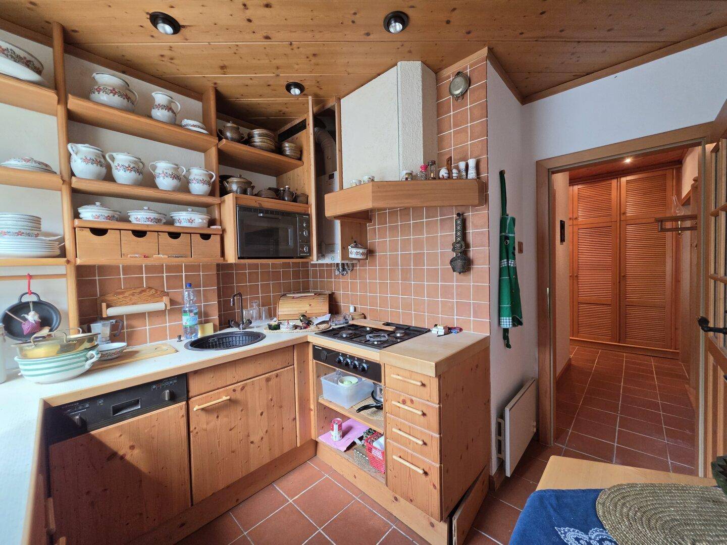 Funktionale Küche mit Holzschränken, Terrakottafliesen und einem Gasherd, ideal für traditionelles Kochen.