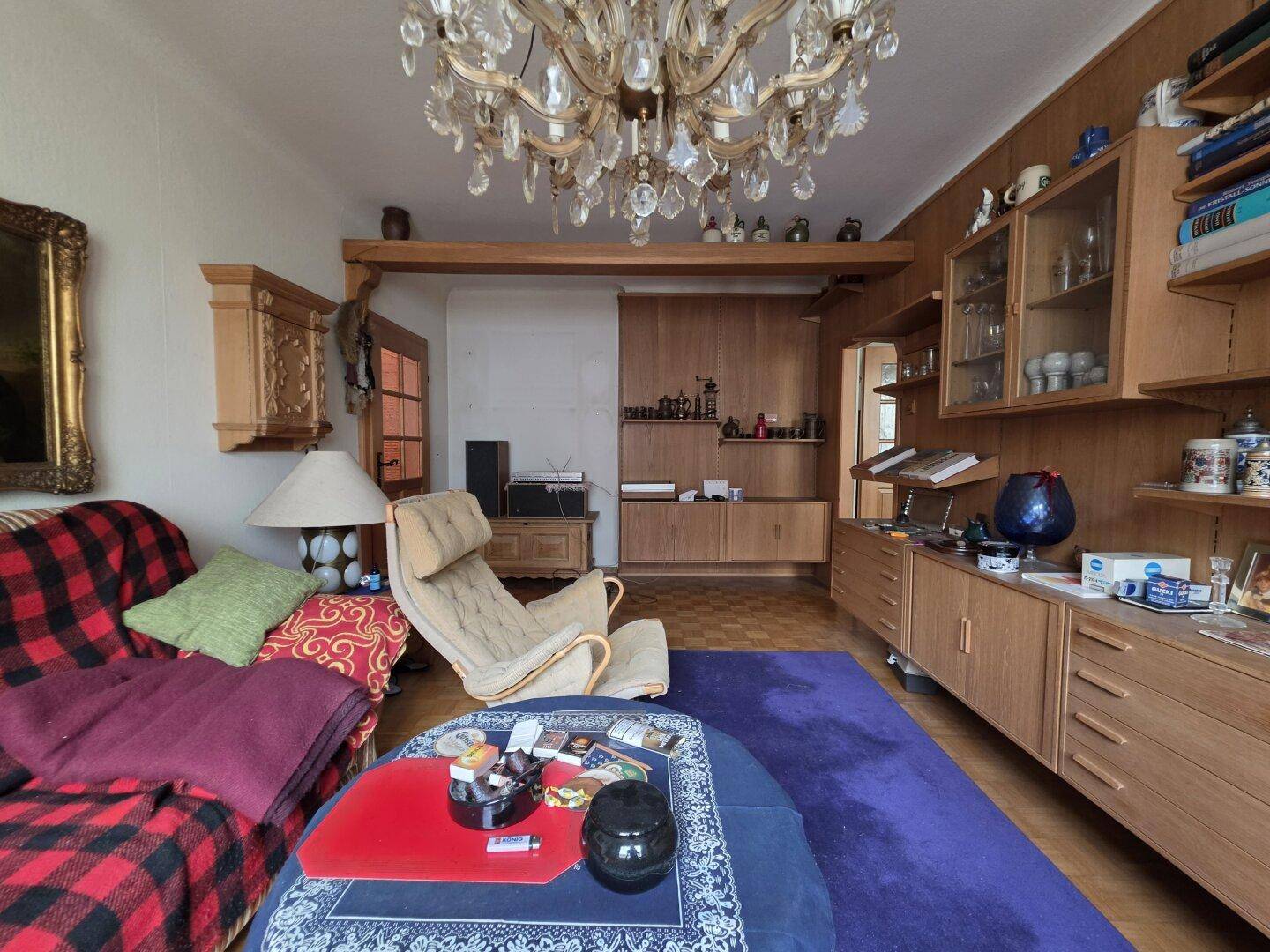 Wohnzimmer mit klassischem Kronleuchter, Holzvertäfelung und bequemen Möbeln, die zum Entspannen einladen.