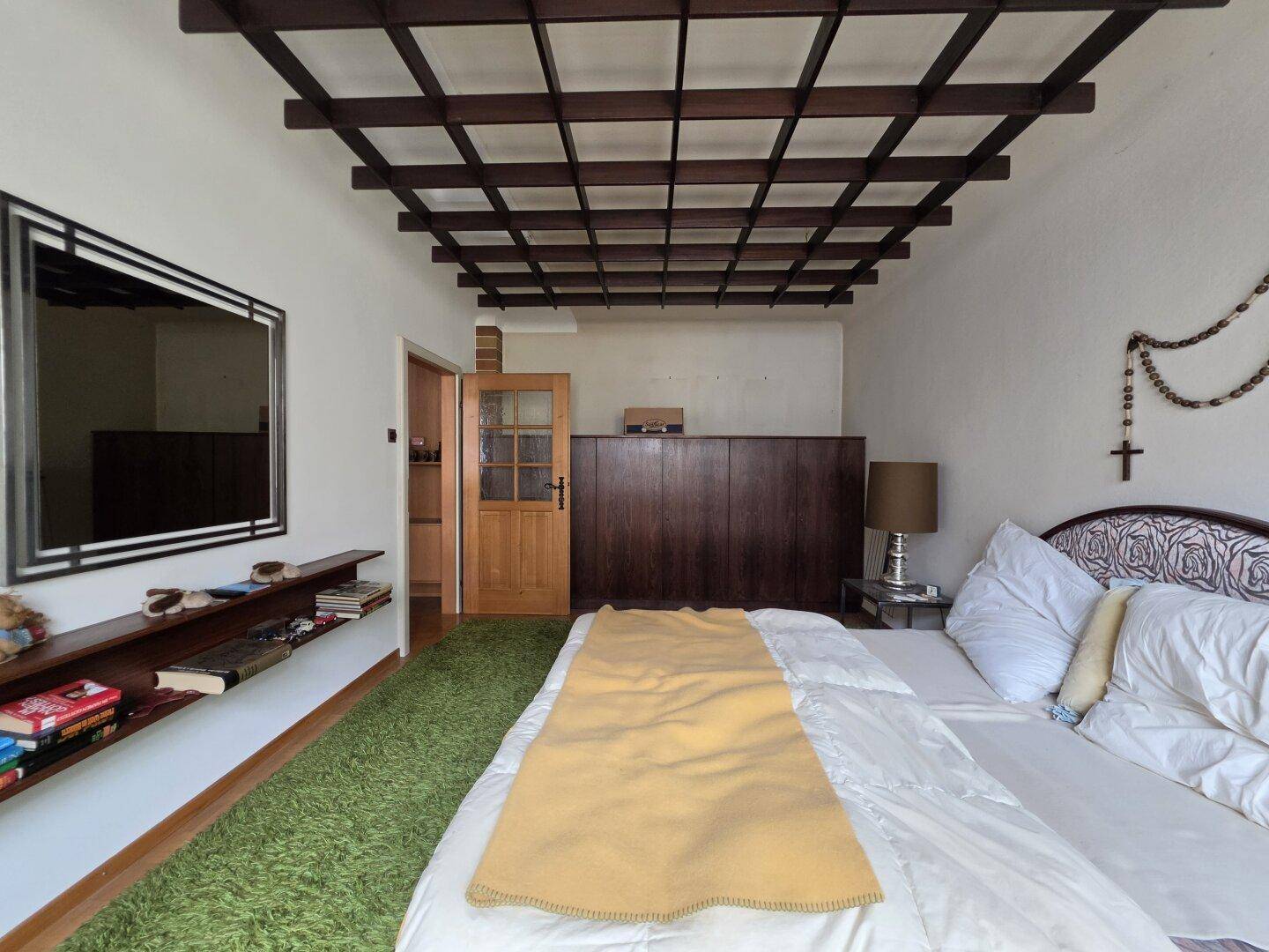 Schlafzimmer mit Gitterdecke, Teppichboden und einer Holztür, das einen traditionellen Charme verleiht.