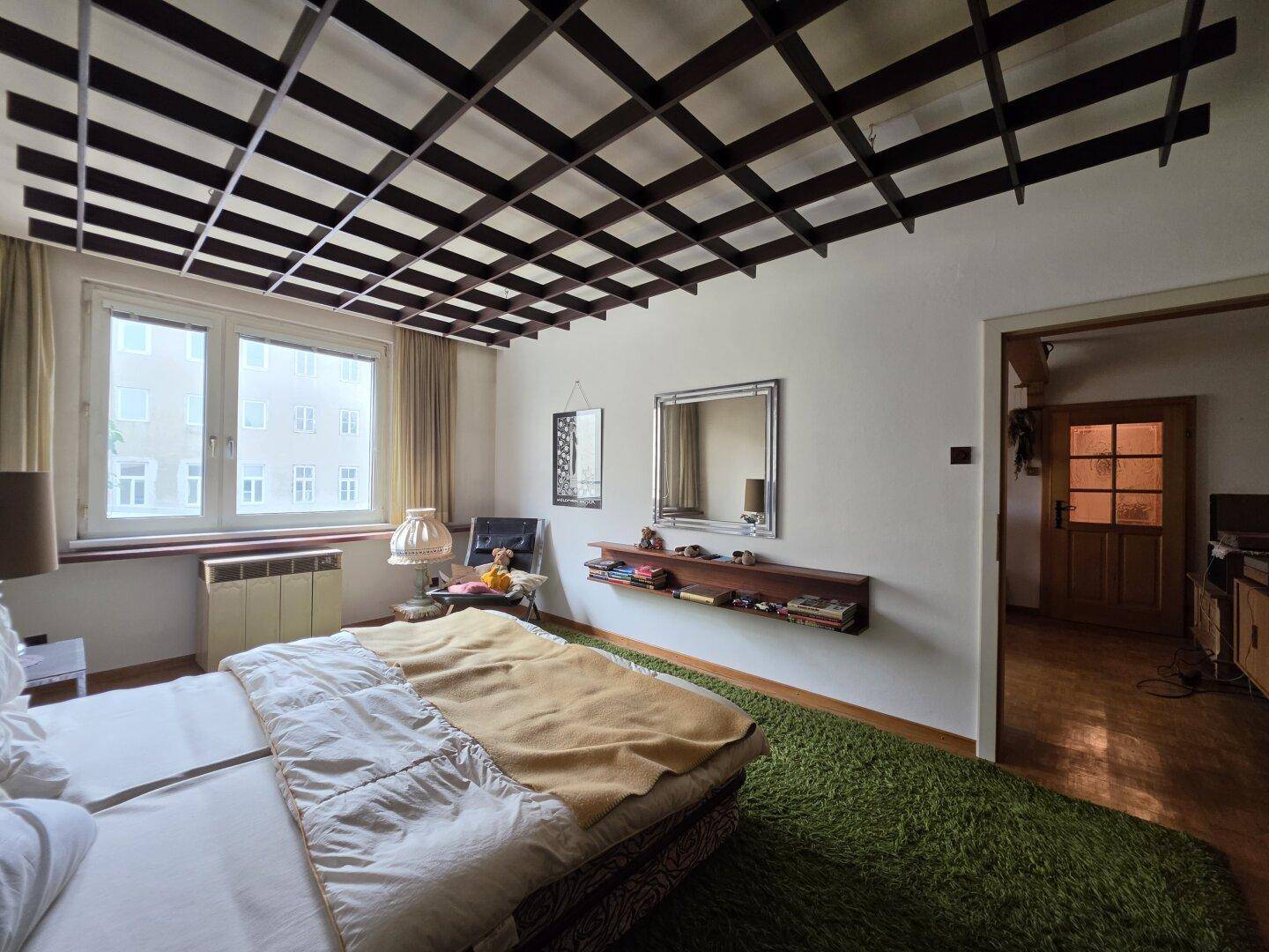 Schlafzimmer mit Gitterdecke, Teppichboden und einem großen Bett, das zum Ausruhen einlädt.