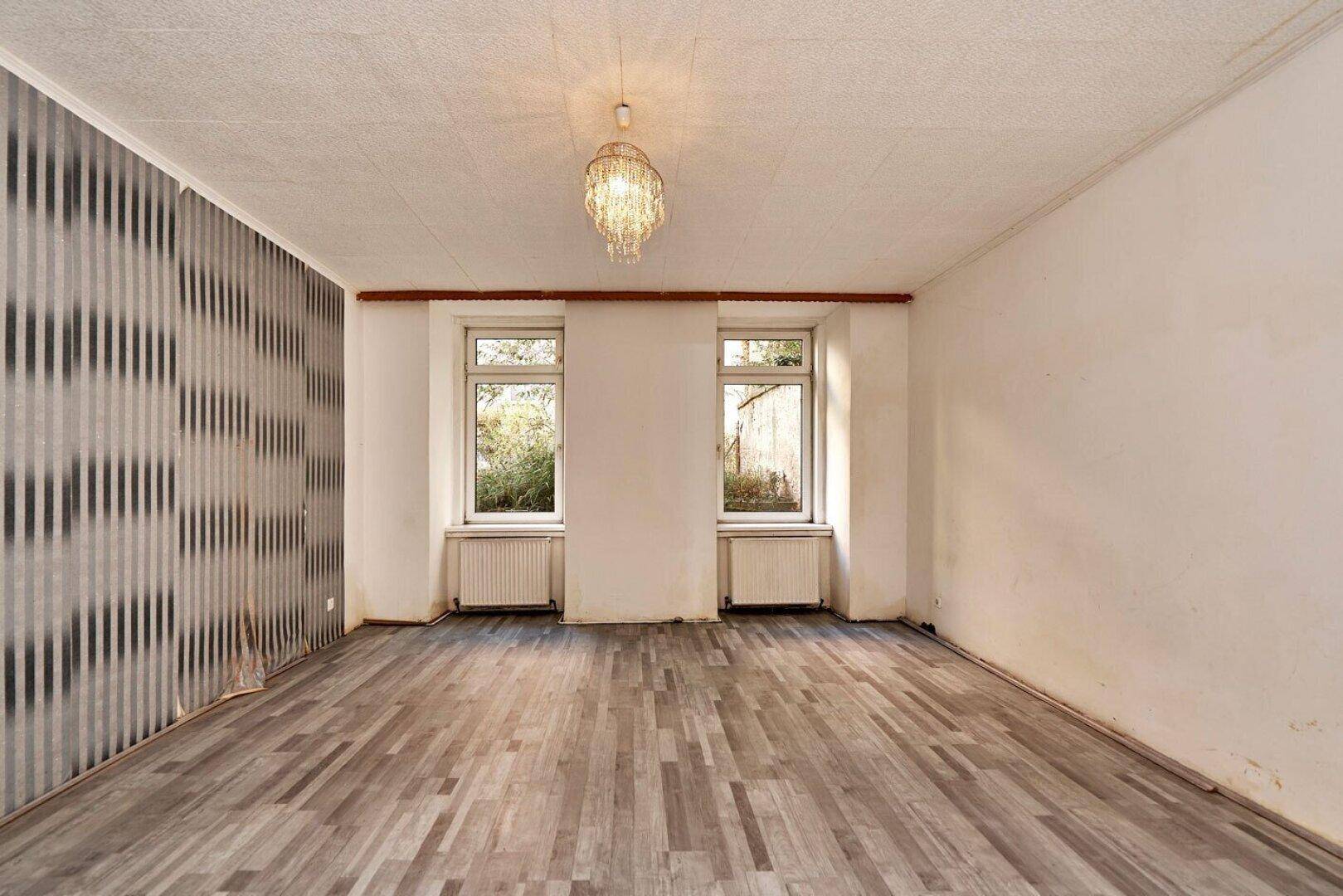 Leerer Raum mit modernem Tapetenakzent, Laminatboden und zwei Fenstern.