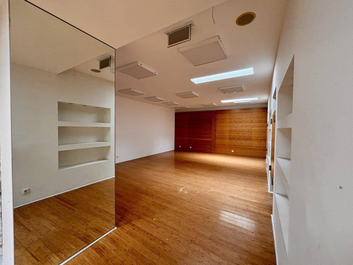 Heller Gewerberaum mit Holzboden, einer großen Spiegelfläche und einer Holzwand im Hintergrund, schafft Weite.