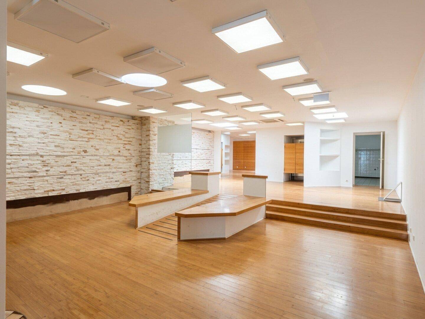 Heller Gewerberaum mit Holzboden, einer strukturierten Wand und modernen Deckenleuchten, bereit zur individuellen Gestaltung.