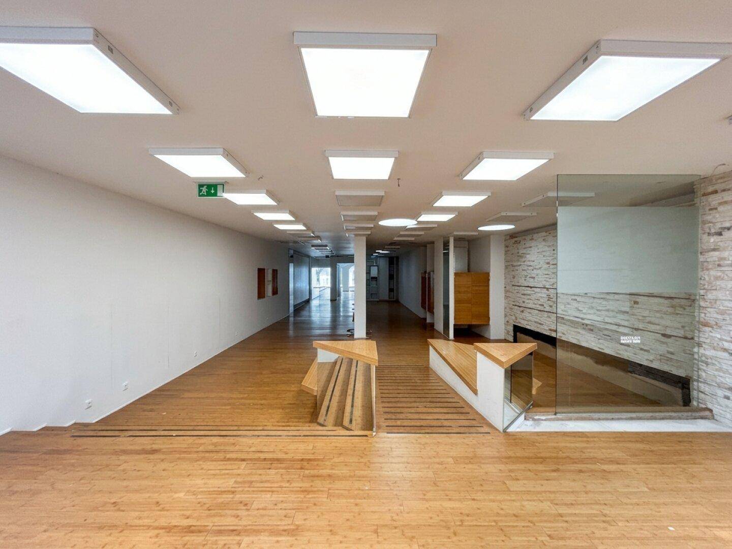 Weitläufiger Verkaufsbereich mit Holzboden, modernen Deckenleuchten und einer eleganten Glasabtrennung.