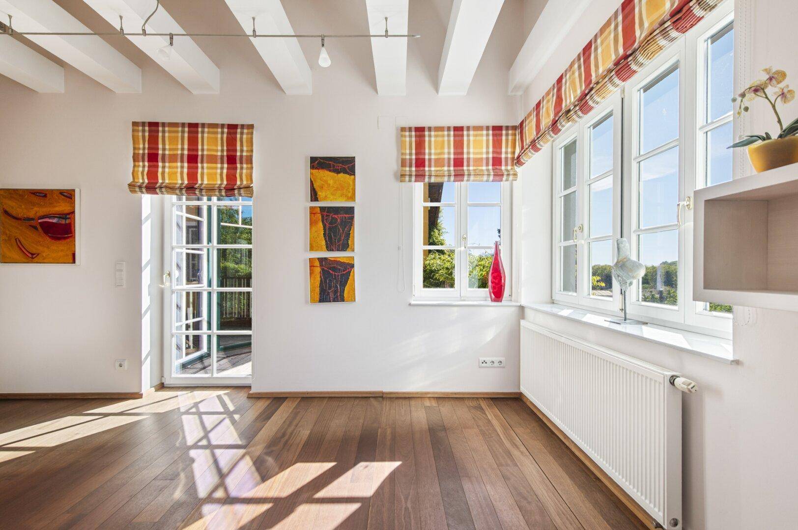 Geräumiges Dachzimmer mit Holzboden, sichtbaren Balken und Zugang zu einem Außenbereich.