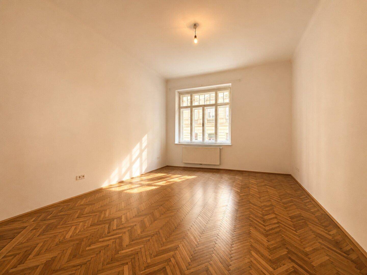 Geräumiger Raum mit klassischem Fischgrätparkett und großem Fenster.