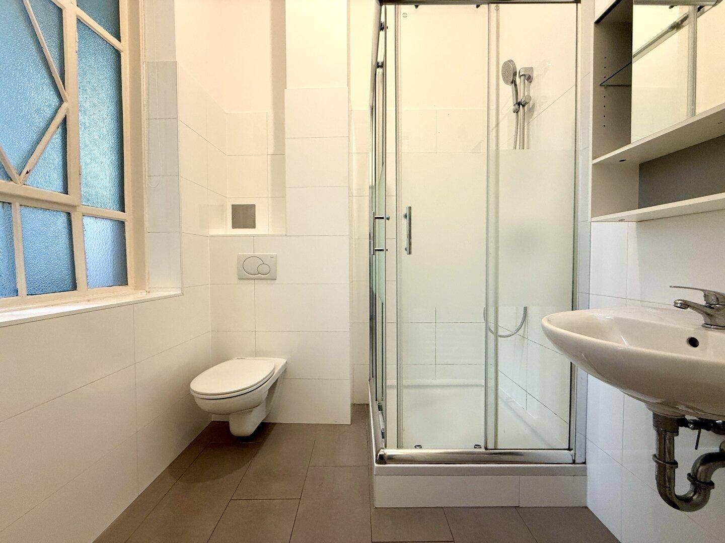 Helles Badezimmer mit Duschkabine, wandhängendem WC und Fenster.