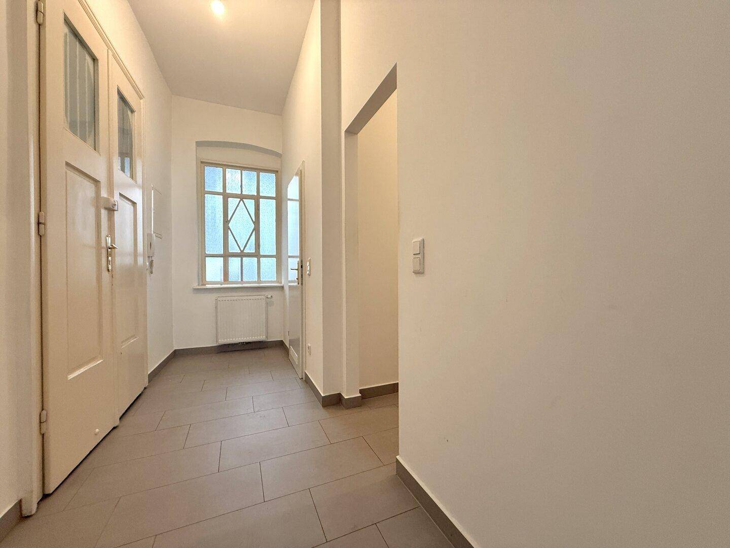 Eingangsbereich mit Fliesenboden, Fenster und Zugang zu verschiedenen Zimmern.