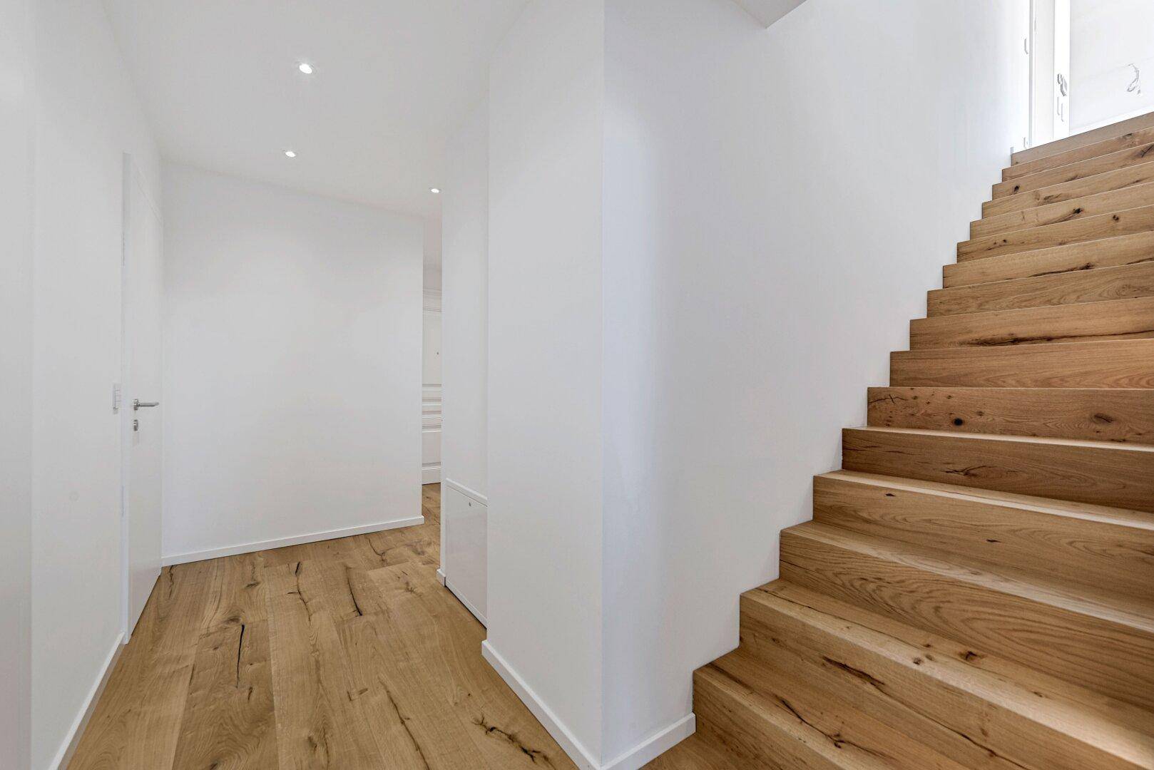 Heller Flur mit Holztreppe und Holzboden, der zu den oberen Etagen führt.
