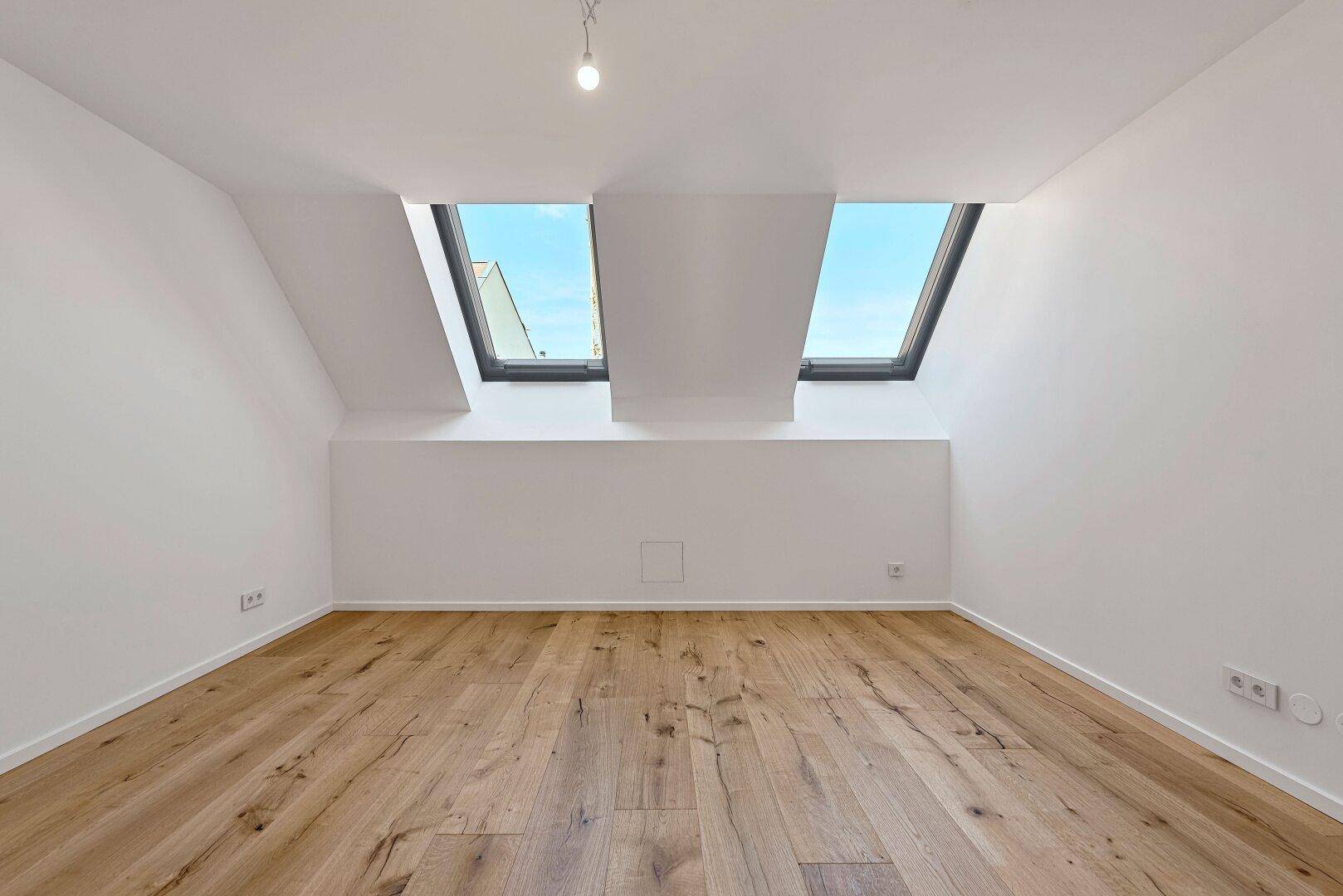 Helles Zimmer mit Holzboden und zwei Dachfenstern, die den Raum erhellen.