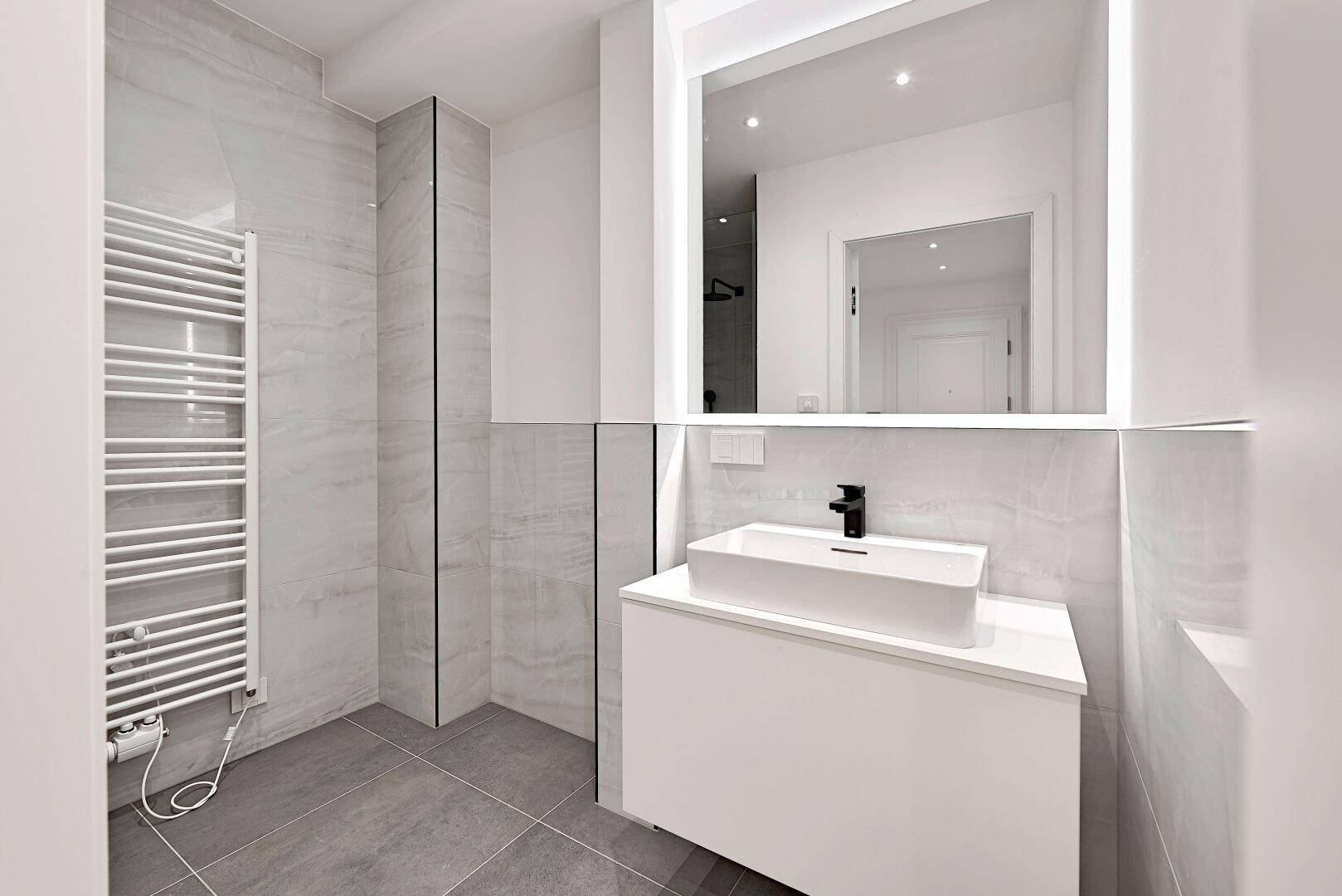 Modernes Badezimmer mit Waschtisch, beleuchtetem Spiegel und beheiztem Handtuchhalter.