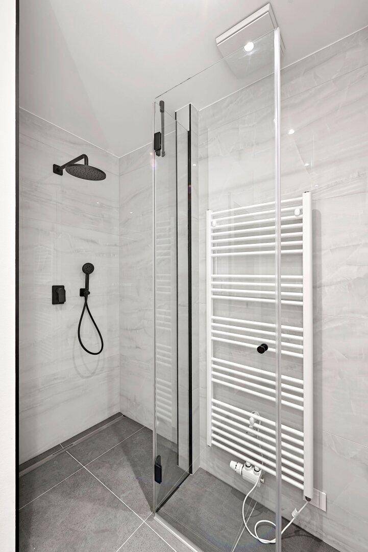 Moderne begehbare Dusche mit schwarzer Armatur und beheiztem Handtuchhalter.