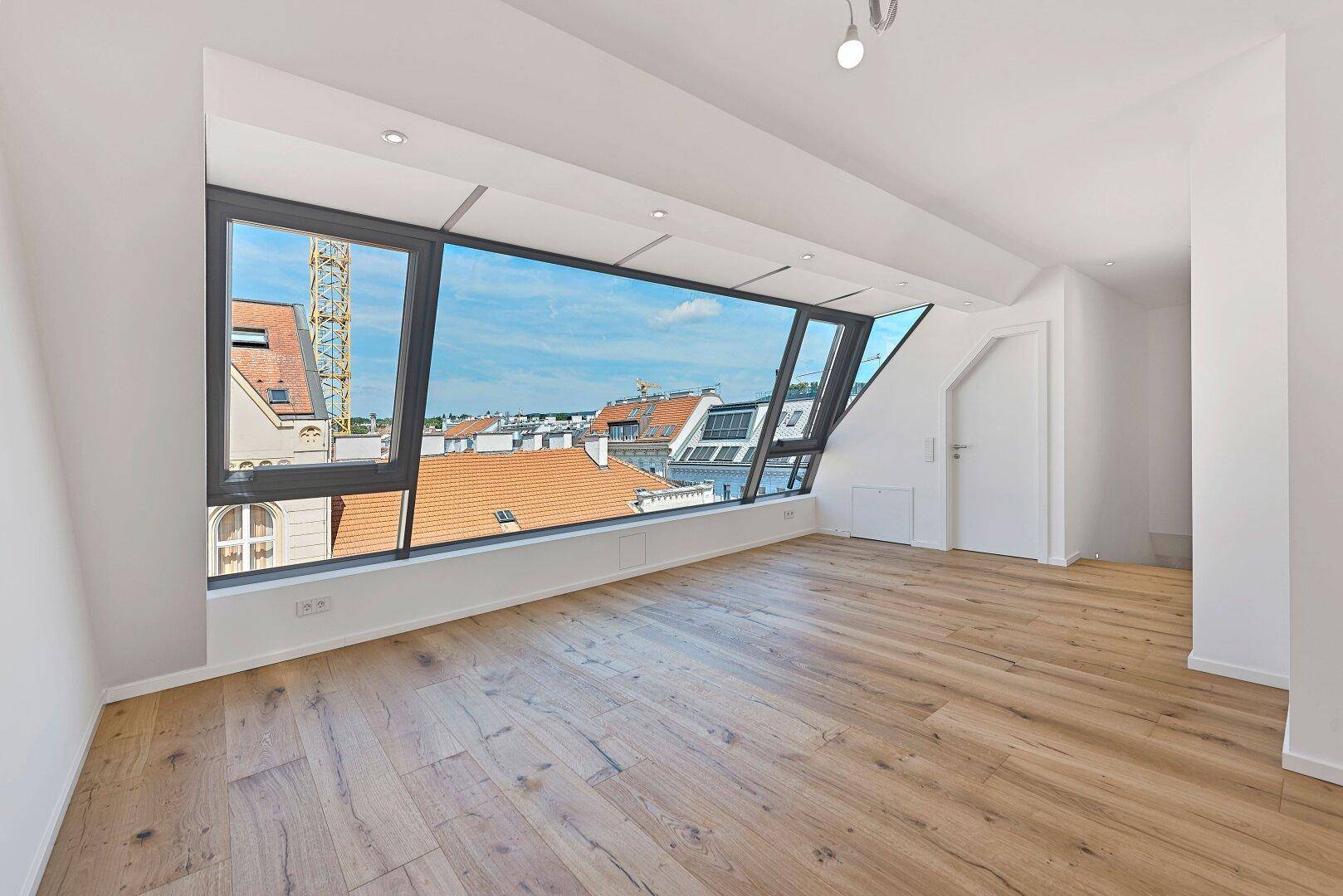 Geräumiges Zimmer mit Holzboden und großer Fensterfront mit Stadtblick.