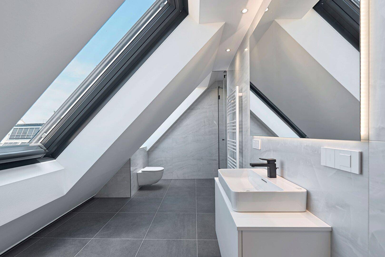 Modernes Badezimmer im Dachgeschoss mit Dachfenster, WC und Waschtisch.