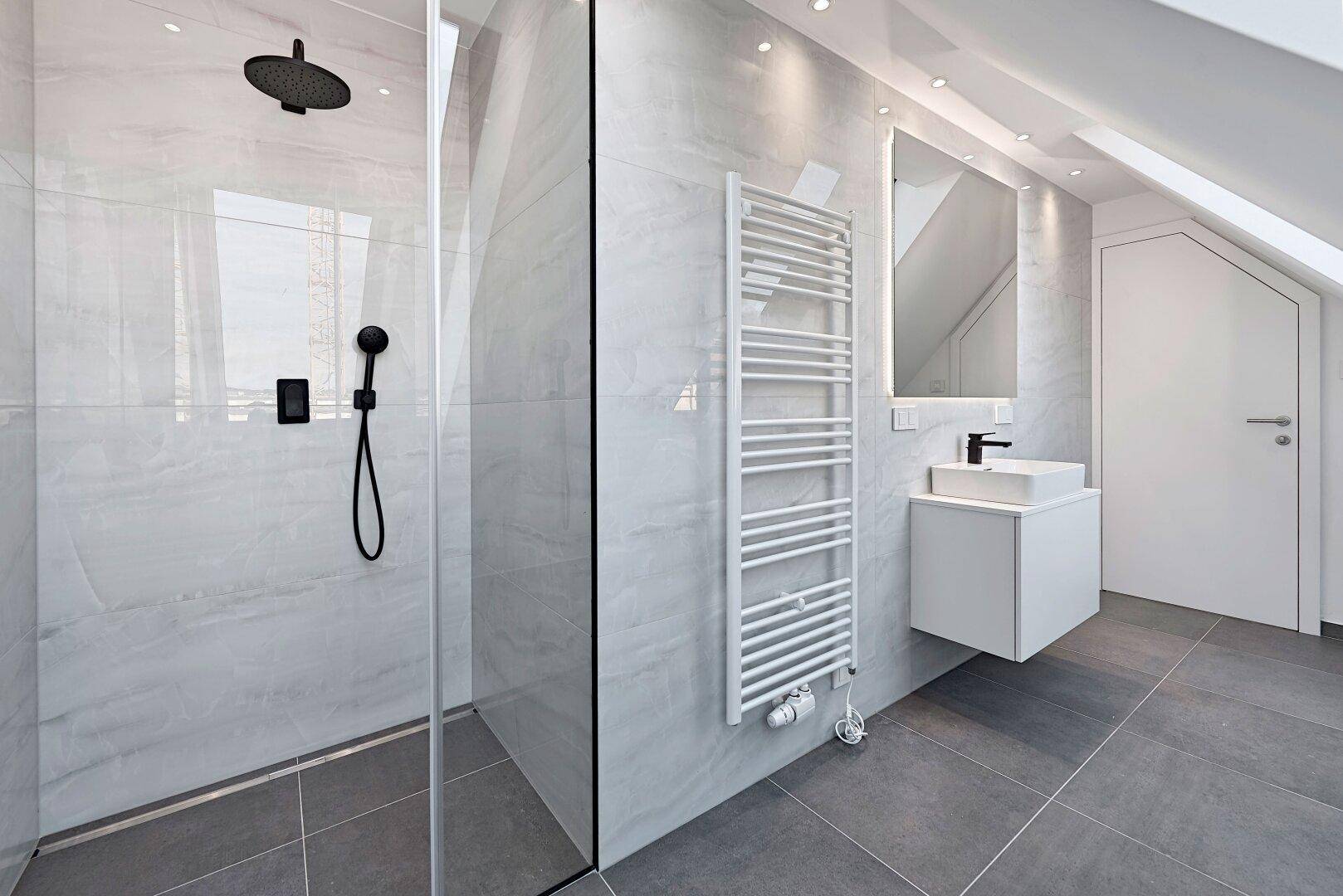 Modernes Badezimmer mit begehbarer Dusche, grauen Fliesen und beheiztem Handtuchhalter.