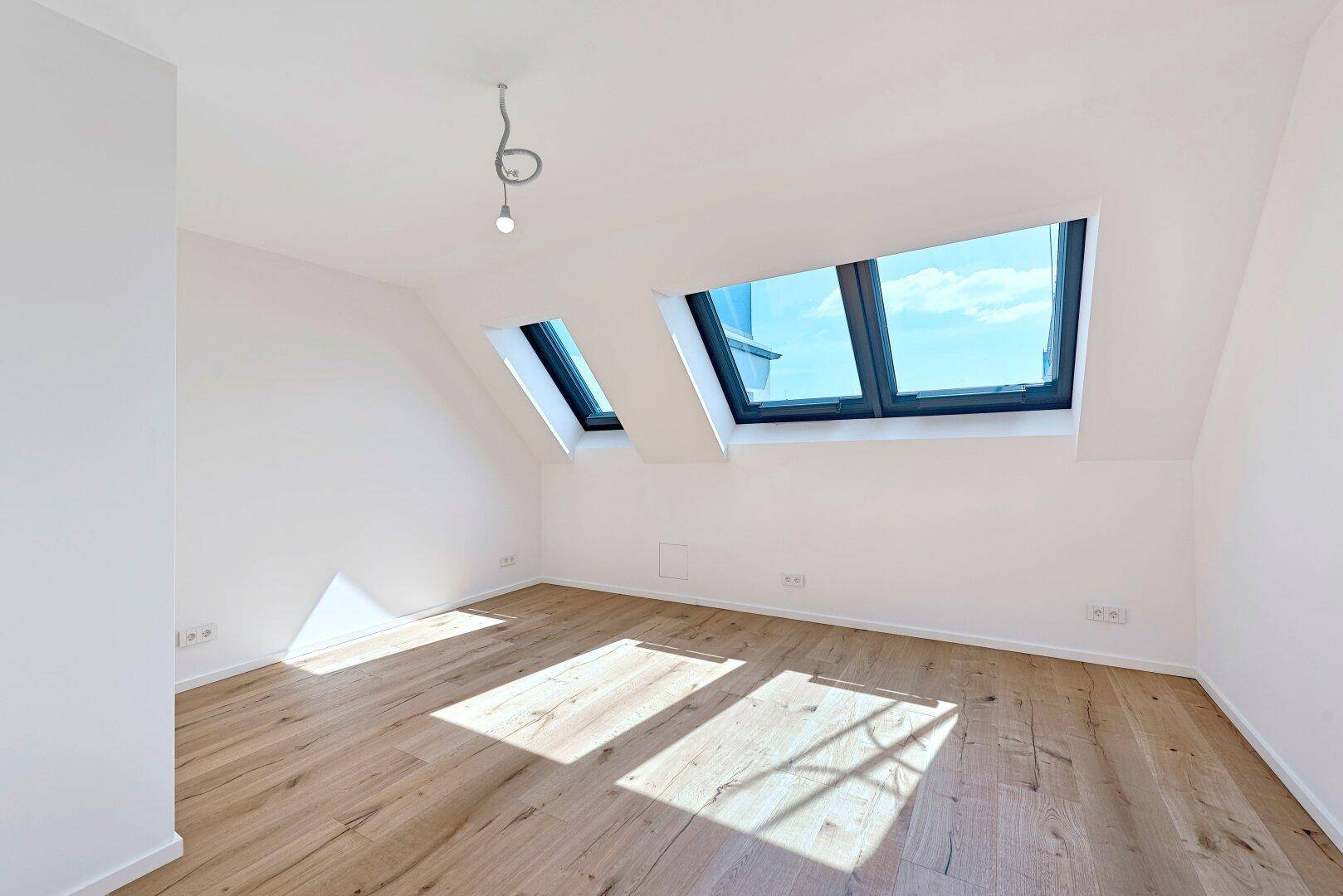 Helles Zimmer mit Holzboden und Dachfenstern, die viel Sonnenlicht hereinlassen.