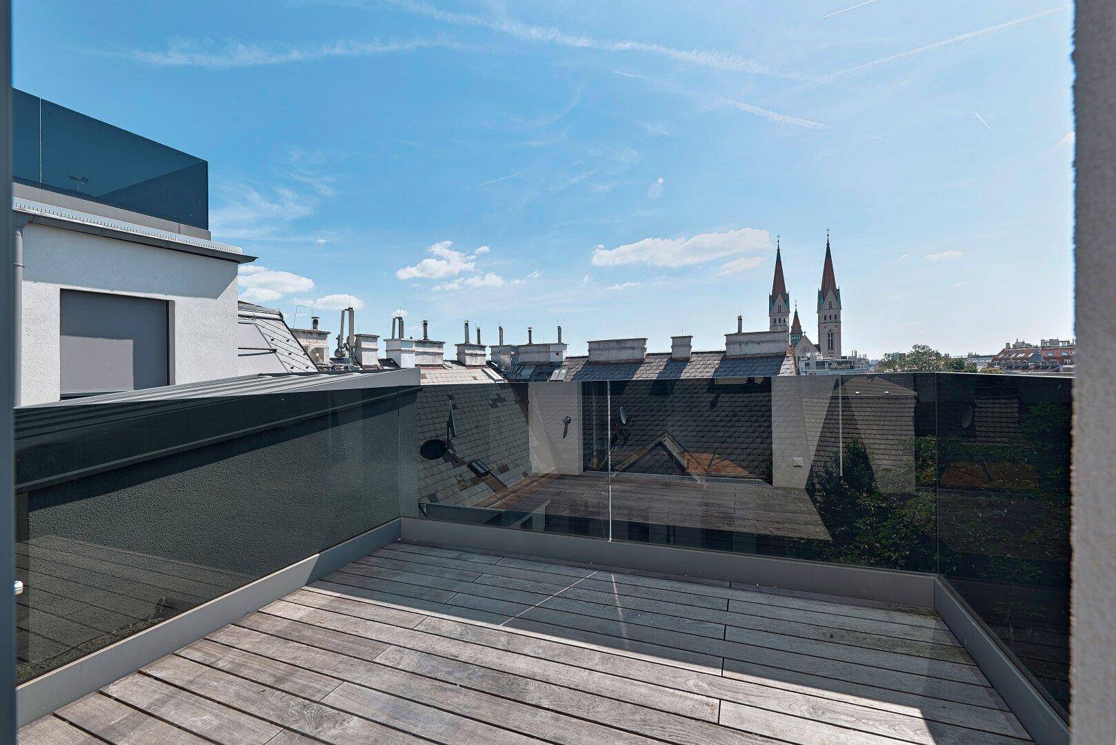 Dachterrasse mit Holzboden und Glasgeländer bietet einen weiten Blick über die Stadt.