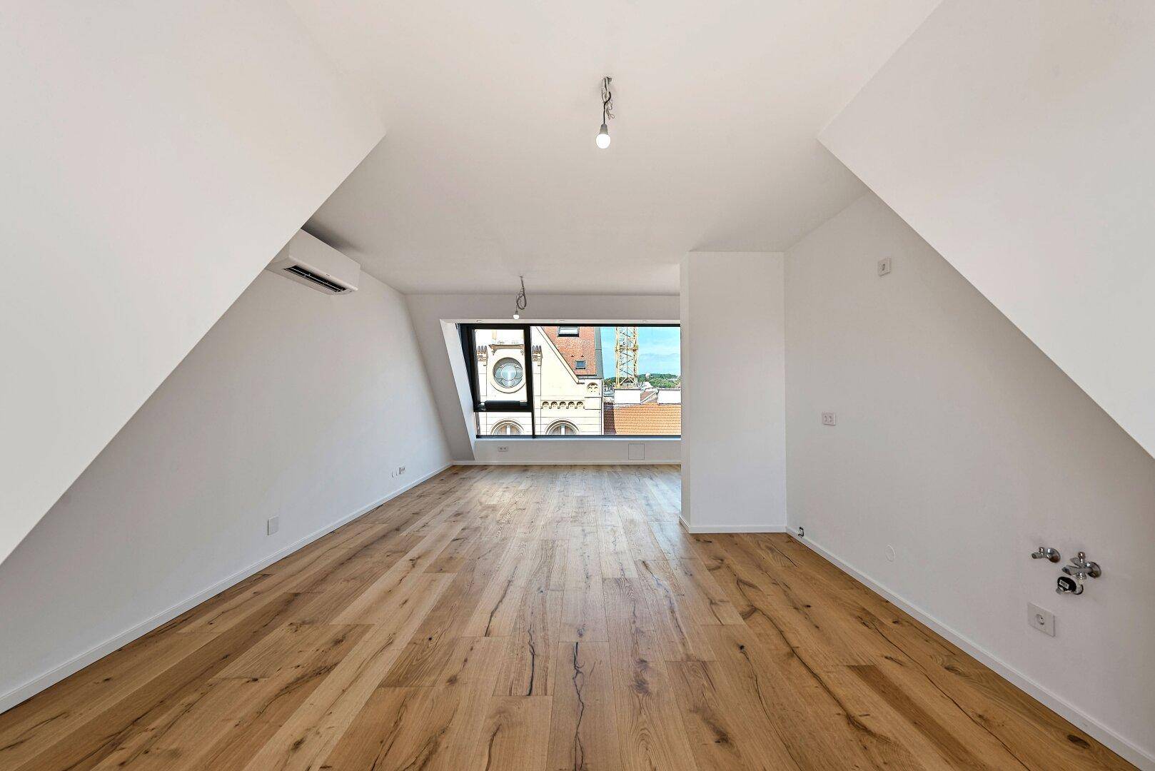 Heller Raum mit Holzboden, Klimaanlage und Fenster mit Blick auf die Stadt.