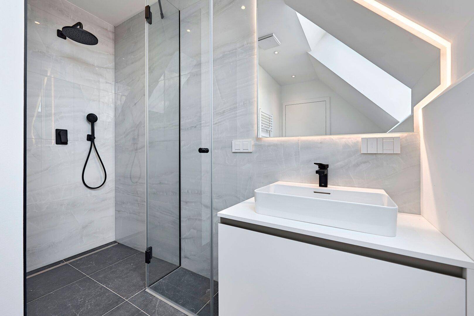 Modernes Badezimmer mit begehbarer Dusche, eleganten Fliesen und beleuchtetem Spiegel.
