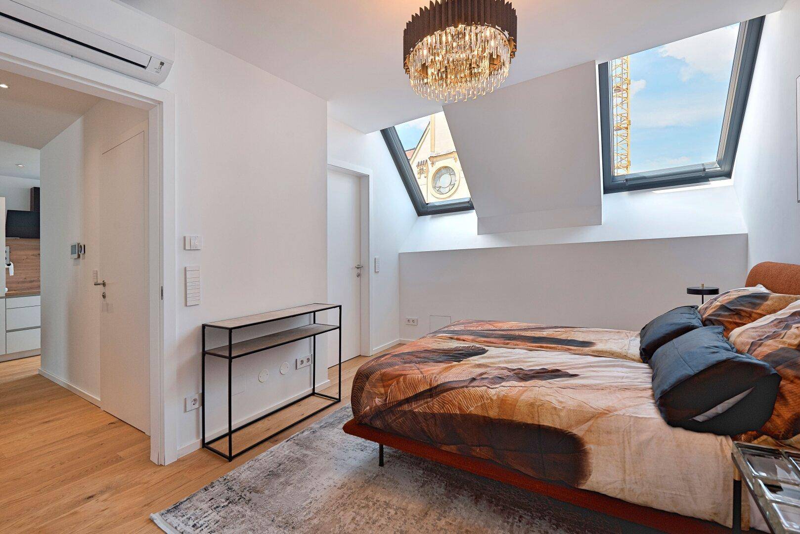 Gemütliches Schlafzimmer mit Holzboden, Dachfenstern und Klimaanlage, bietet viel Tageslicht.