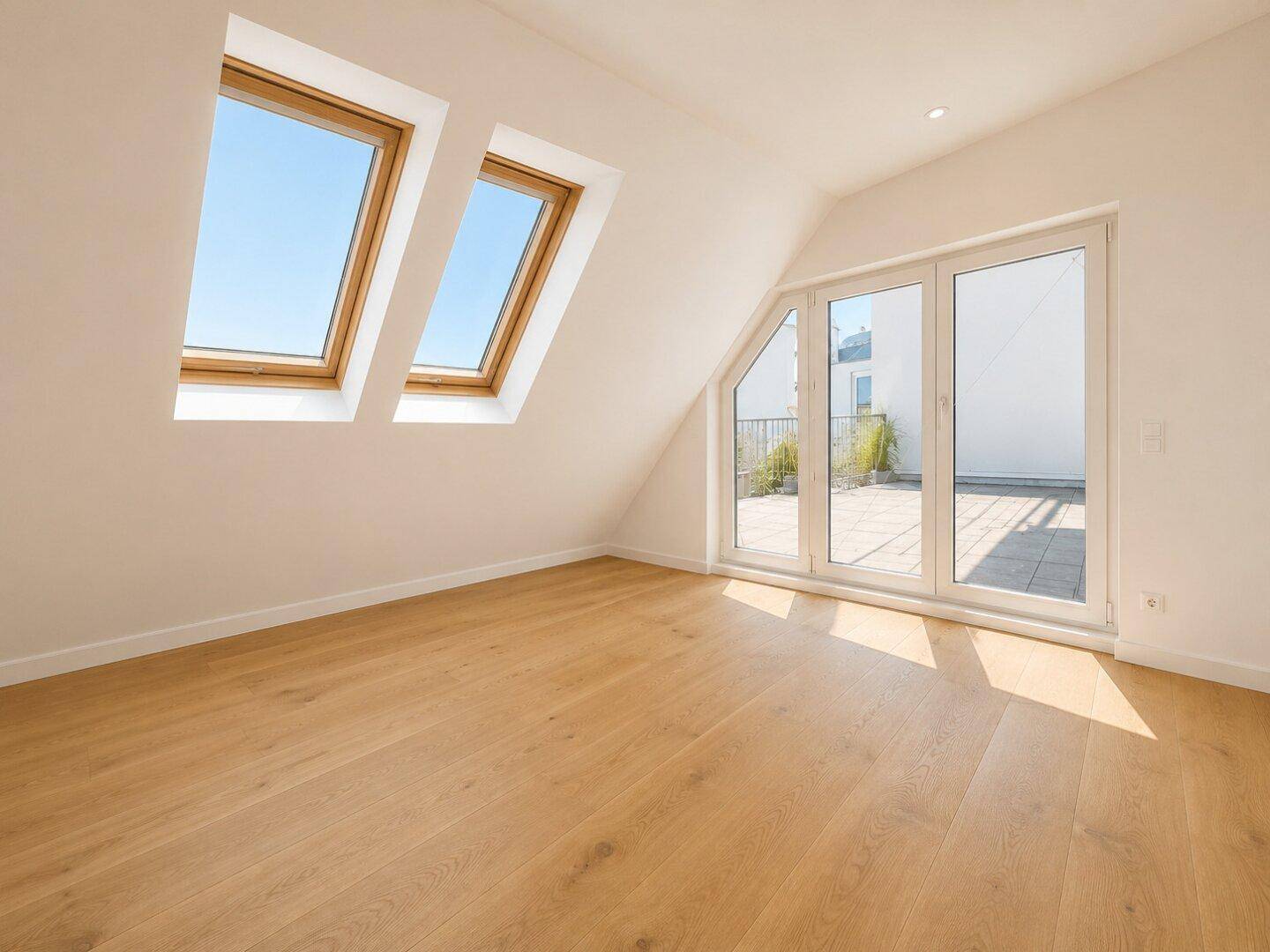 Heller Raum mit Holzboden, Dachschrägen und großen Dachfenstern, mit Zugang zur Terrasse.