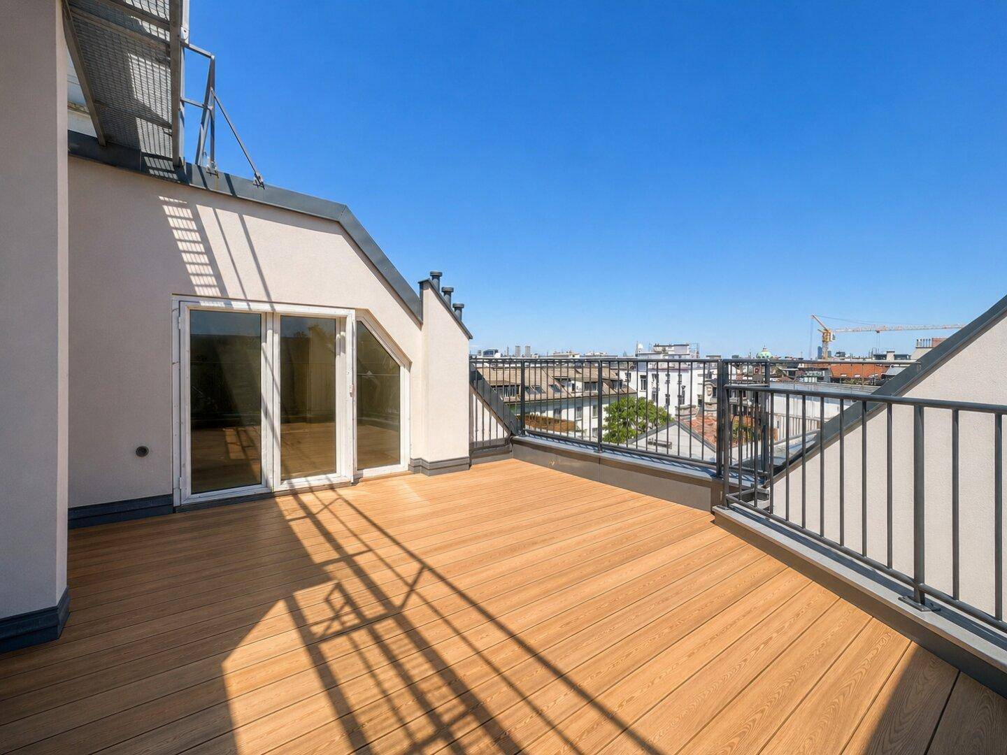 Geräumige Dachterrasse mit Holzboden und Blick über die Stadt, zugänglich durch eine Glastür.