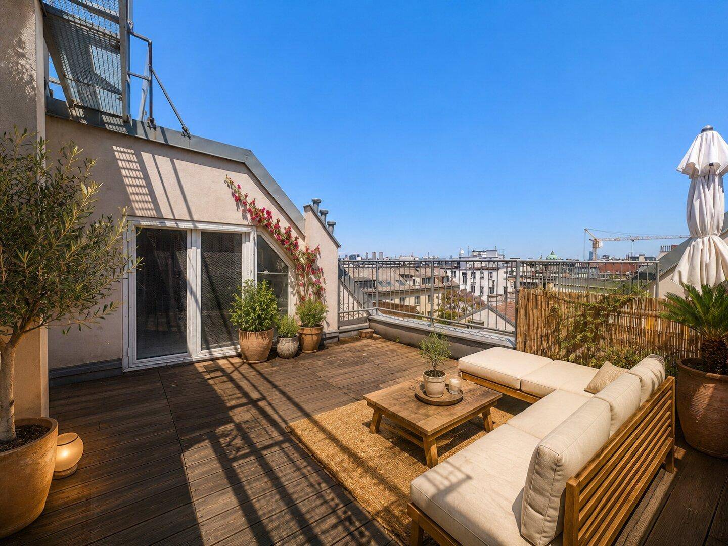 Möblierte Dachterrasse mit Holzboden, bequemen Sitzgelegenheiten und Pflanzen, ideal zum Entspannen.